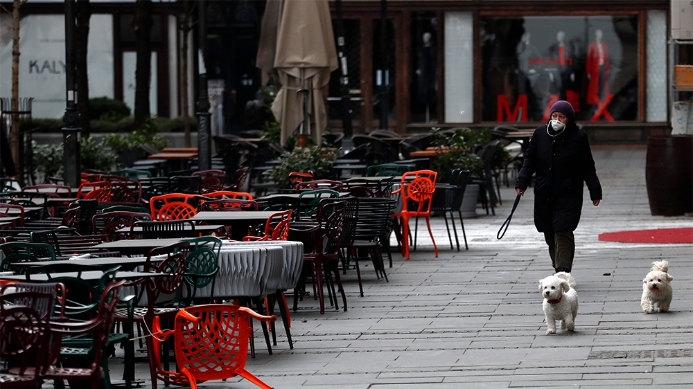 A woman walks with dogs in a deserted street amid the coronavirus outbreak in downtown Belgrade, Serbia, Thursday, March 26, 2020. (AP Photo/Darko Vojinovic)