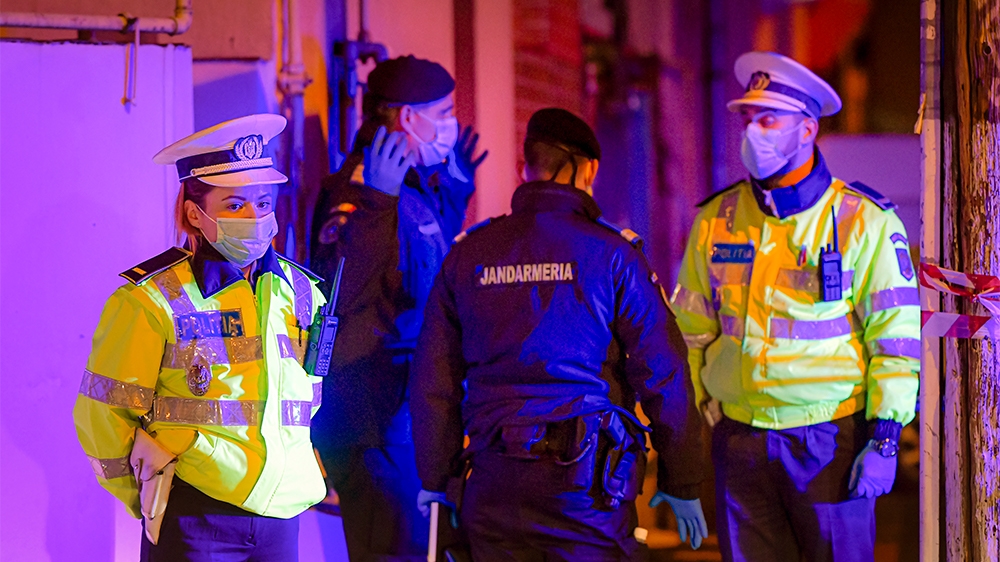 Illuminated by police car lights, a female police officer, left, wearing a protective mask stands at a roadblock in the vicinity of one of the hospital where COVID-19 infected patients are under trea