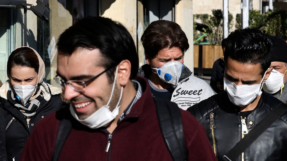 People wearing face masks walk on a sidewalk, in downtown Tehran, Iran, Monday, March 2, 2020. A member of a council that advises Iran's supreme leader died Monday after falling sick from the new coro