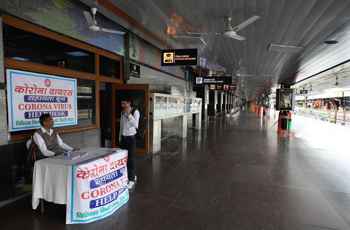 FILE- In this Monday, March 23, 2020, file photo, an Indian railways employee sits at a coronavirus help desk at the deserted New Delhi Railway station during a lockdown amid concerns over the spread