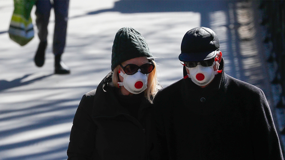 Two people wearing masks walk in Regents Park in London, Monday, March 23, 2020. The British government is encouraging people to practice social distancing to help prohibit the spread of Coronavirus,
