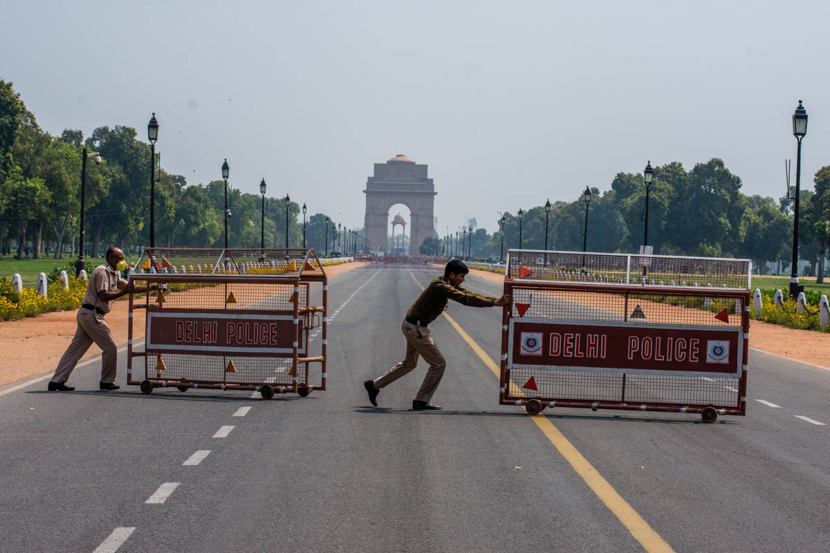 NEW DELHI, INDIA - MARCH 22: Indian policemen push barricades to place them in the center of a a road leading to historic India Gate, during a one-day nationwide Janata (civil) curfew imposed as a pr