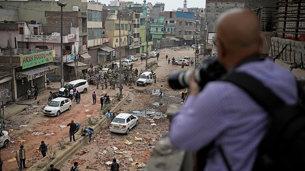 In this Thursday, Feb. 27, 2020 photo, a photojournalist takes photographs of Indian paramilitary soldiers patrolling a street vandalized in Tuesday''s violence in New Delhi, India. Reporting in India