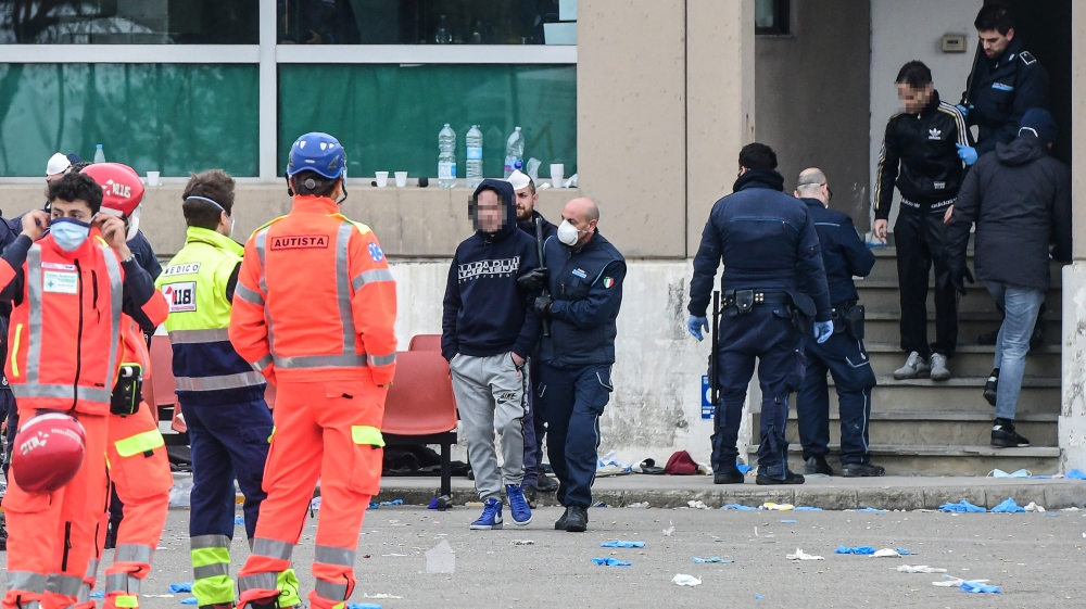A prison guard wearing a respiratory mask (C) escorts an inmate across a yard of the Sant''Anna prison in Modena, Emilia-Romagna, as some inmates are transfered from a building to another, in one of It