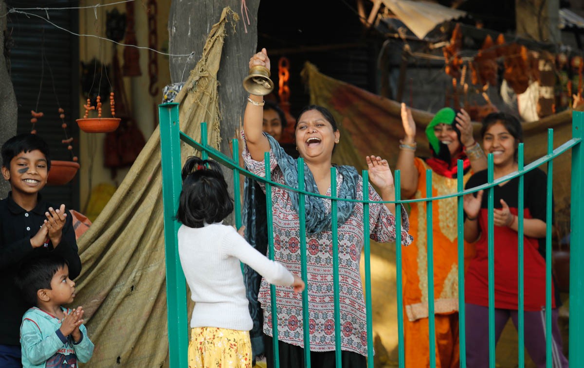 Families of roadside shopkeepers ring bell and clap to cheer health workers following coronavirus outbreaks, in New Delhi, India, Sunday, March 22, 2020. India is observing a 14-hour "people''s curfew"