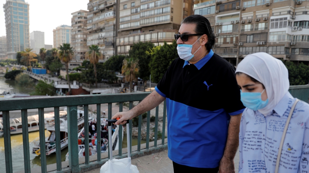People wearing protective face masks due to the spread of coronavirus disease (COVID-19), pass near people who celebrate a wedding party on a yacht along the bank of the Nile river