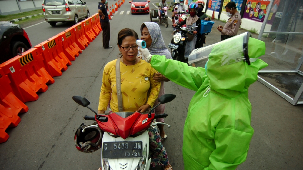 A medical officer wearing a protective suit checks a woman with a thermal scanner amid the coronavirus disease (COVID-19) outbreak in Tegal