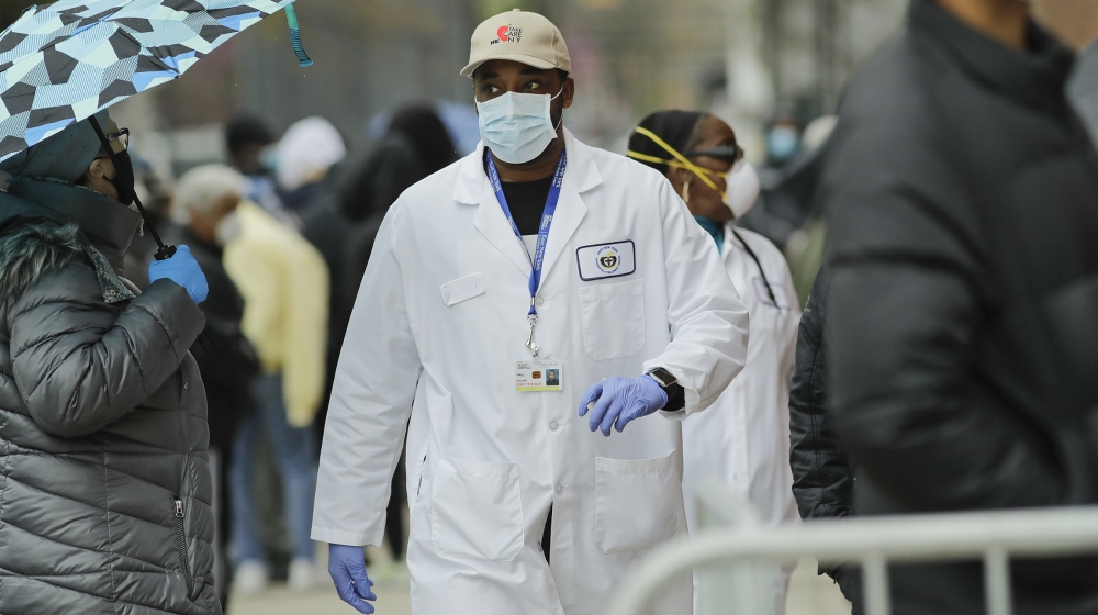 A medical worker walks past people lined up at Gotham Health East New York, a COVID-19 testing center Thursday, April 23, 2020, in the Brooklyn borough of New York. (AP Photo/Frank Franklin II)