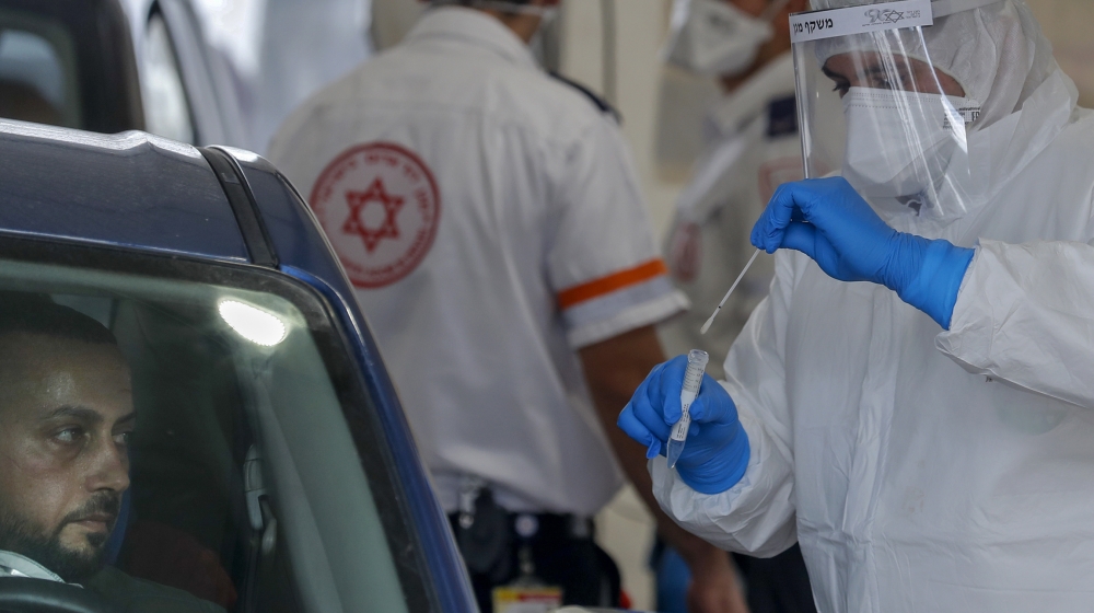 A Paramedic with Israel''s Magen David Adom (Red Shield of David) national emergency medical service, puts a swab into a tube after using it to test a man for COVID-19, at a drive-thru testing site in