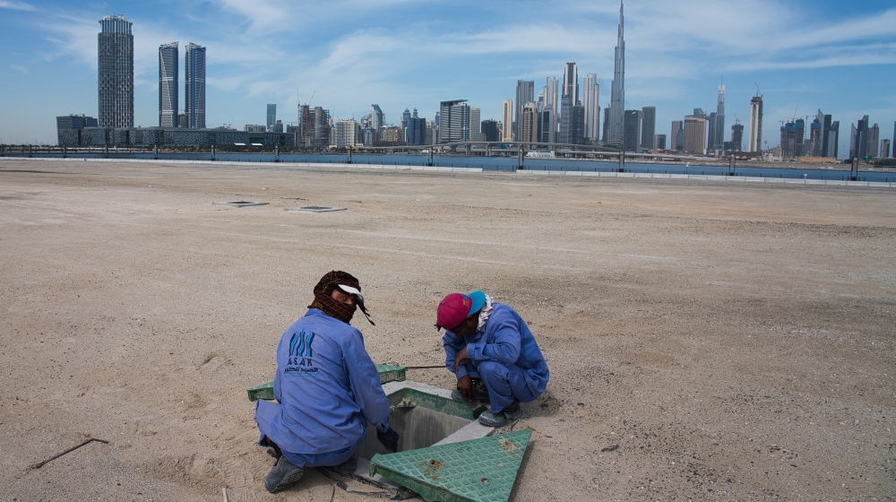Two construction workers examine a drainage system with the Burj Khalifa, the world''s tallest building, in the skyline behind them in Dubai, United Arab Emirates, Monday, April 6, 2020. Dubai, one of