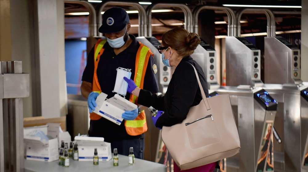 An MTA worker hands out free hand sanitizer and face masks at the Grand Central Station subway during morning rush hour on June 8, 2020 in New York City. Today New York City enters 