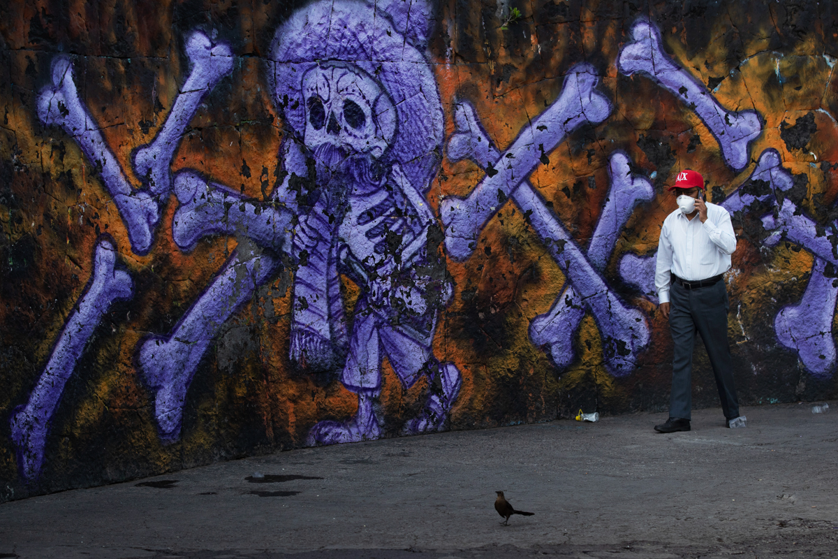 Arturo Morales Torres, the coordinator of several public cemeteries, talks on his cell phone past a mural of a skeleton and bones that decorate the exterior of the Panteón San Nicolás Tolentino de Izt