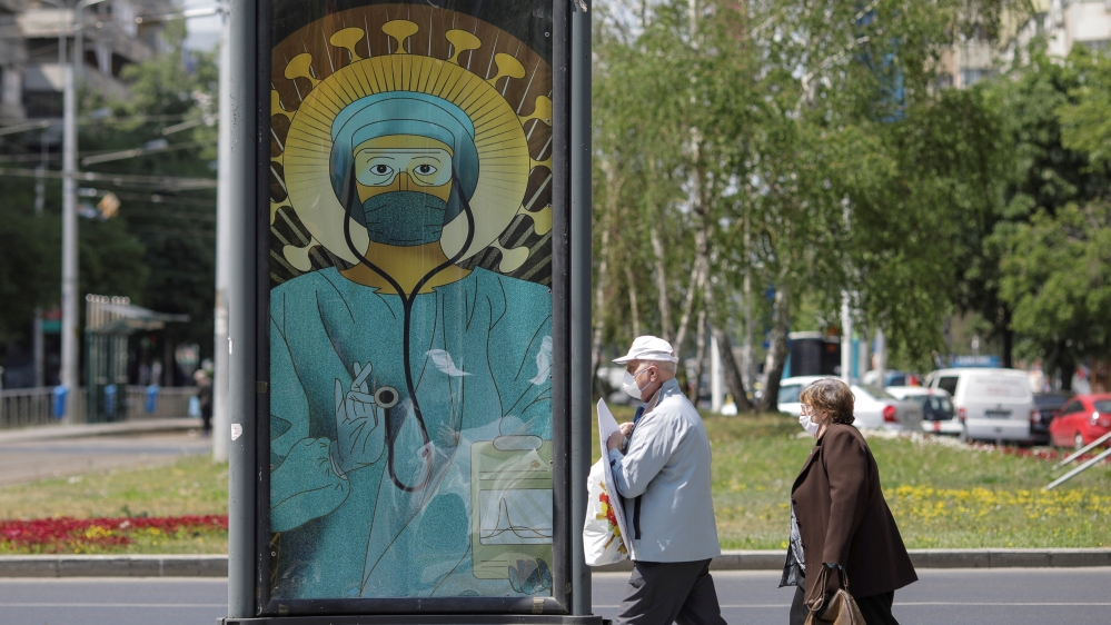 People pass by an outdoor poster that shows a medic depicted in a similar manner as Jesus Christ would be portrayed by Christian Orthodox religious paintings