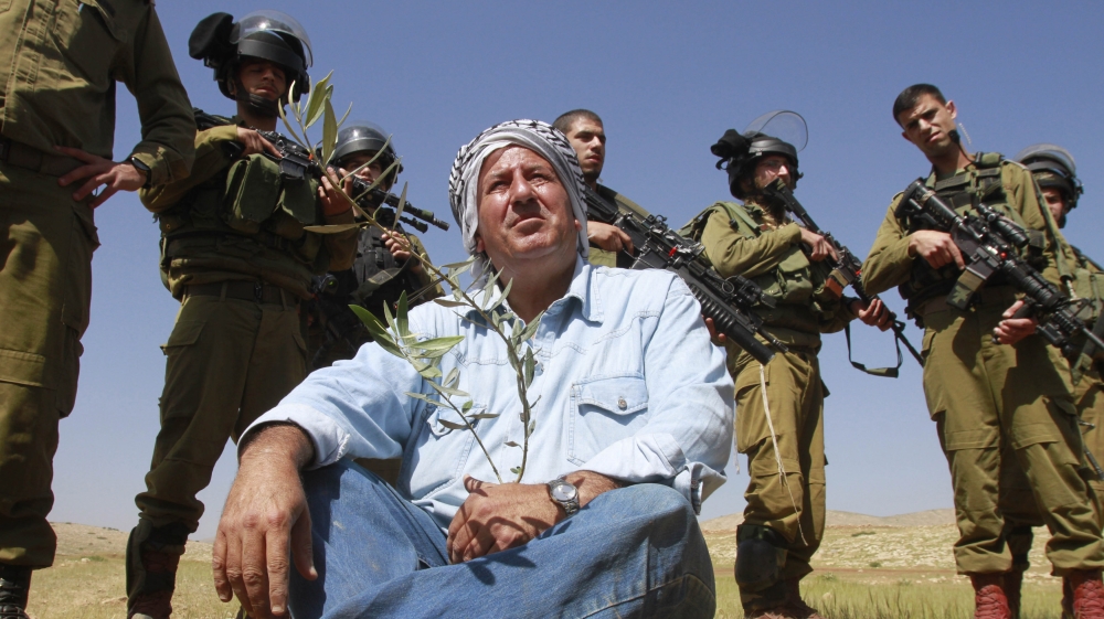 Israeli soldiers stand guard as a Palestinian farmer sits on the ground after planting olive trees during a protest in the Jordan Valley