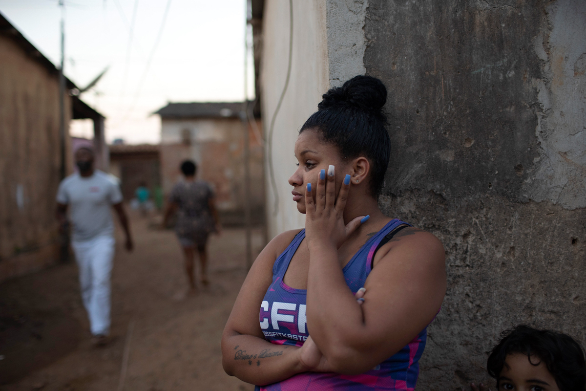 A woman stands against a wall during the distribution of donated food, kits of cleaning products, and protective face masks amid the new coronavirus pandemic, at the Maria Joaquina "Quilombo" in Cabo