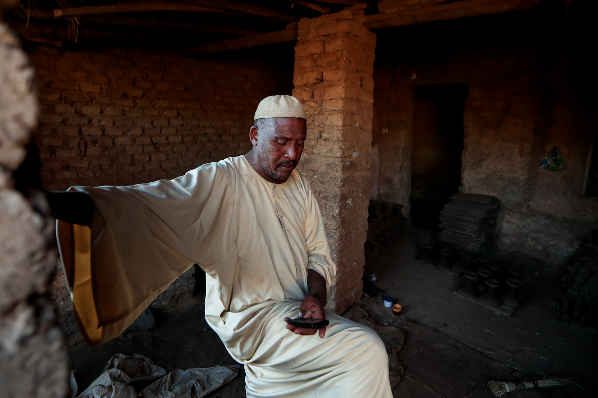 Mutasim al-Jeiry, 50, a pottery maker, checks his mobile phone as he sits inside his workshop in an area known as the "Potters Village" in Alqamayir, Omdurman, Sudan, February 17, 2020. The dam "will