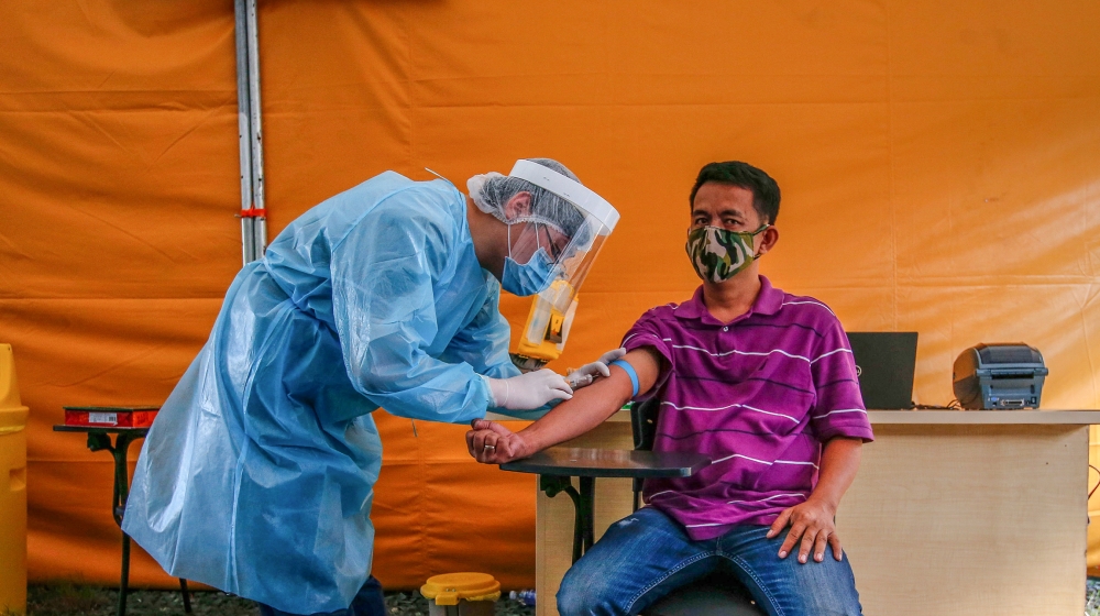 A health worker performs an Enhanced Chemiluminescence Immunoassay (ECLIA) antibody test on a man at a drive-thru COVID-19 testing facility at the Medical City in Ortigas, east of Manila, Philippines,