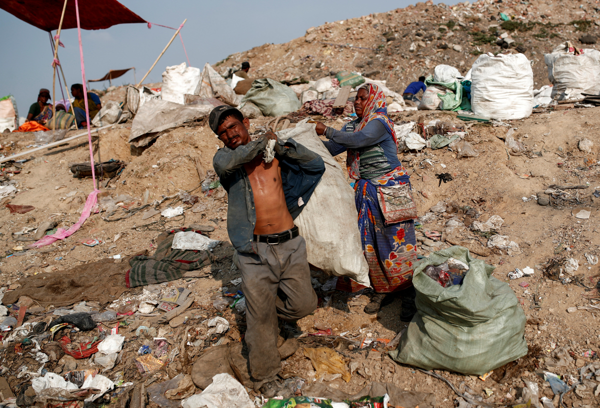 Latifa Bibi, 38, helps her husband Mansoor Khan, 44, a waste collector, carrying a sack of recyclable materials that they found at a landfill site, after finishing work for the day, during the coronav