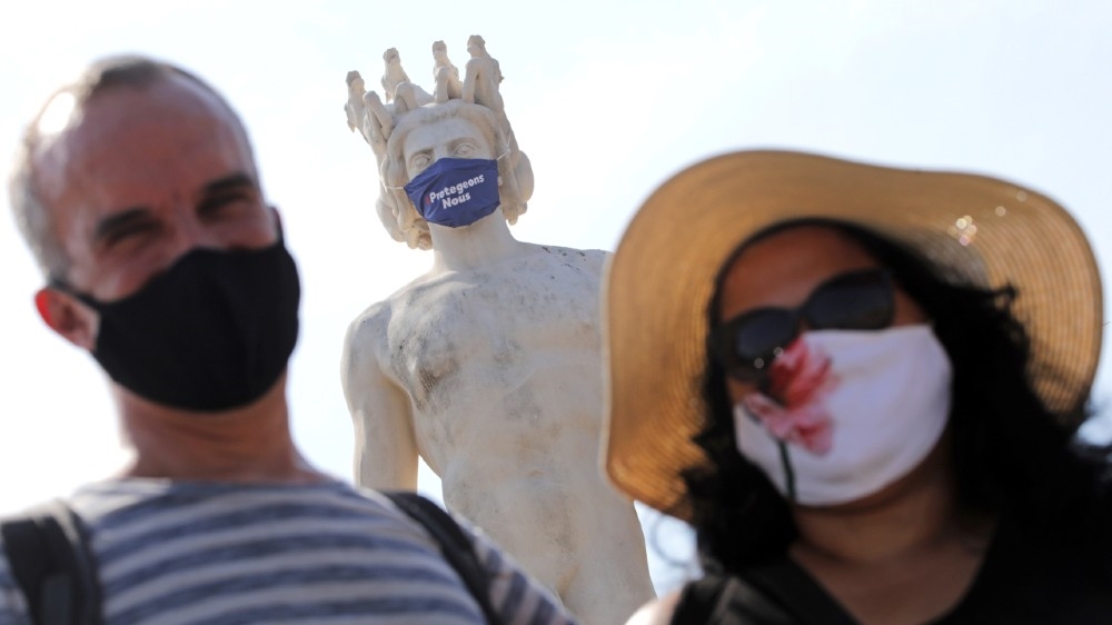Tourists in protective masks stand by a masked statue that reads, 