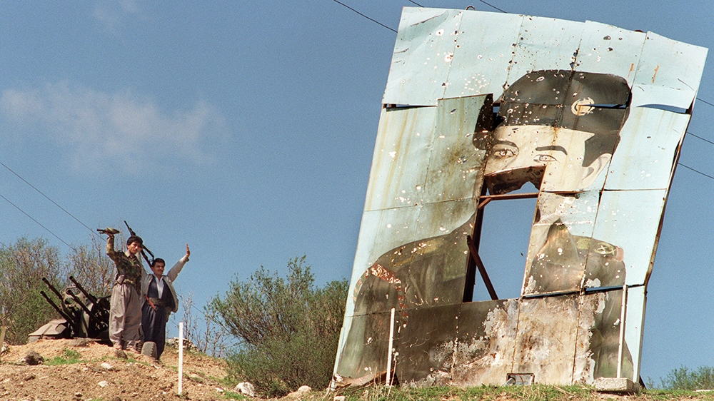 (FILES) In this file photo taken on March 26, 1991, two Kurdish peshmerga rebels stand at their position near at a huge billboard of Iraqi President Saddam Hussein in Dohuk, as fighting intensifies be
