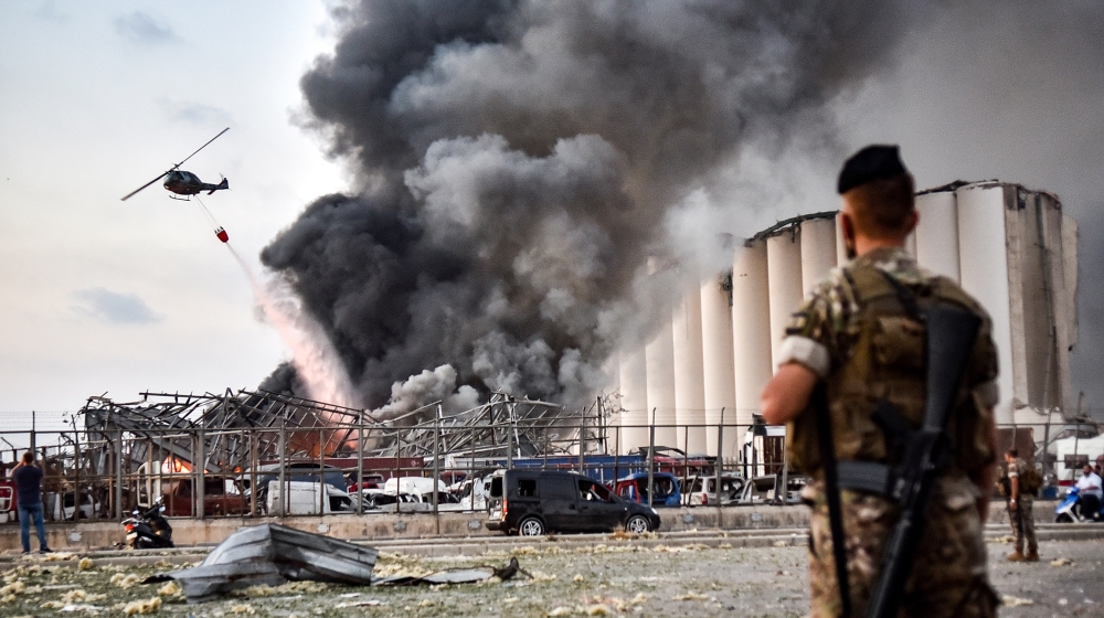 Lebanese army soldiers stand while behind a helicopter puts out a fire at the scene of an explosion at the port of Lebanon's capital Beirut on August 4, 2020. STR / AFP