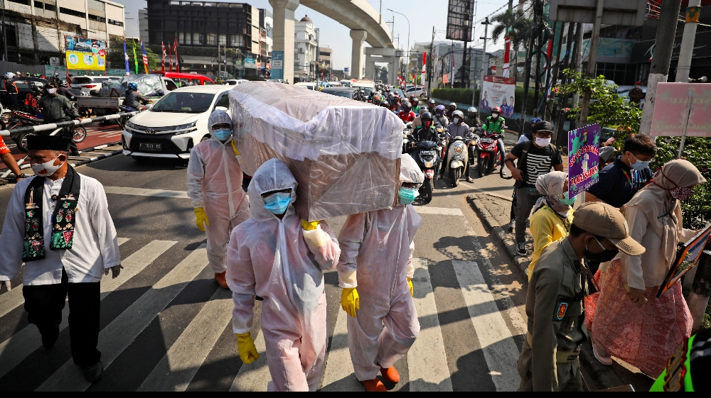 Government officials in protective suits carry a mock coffin as they walk around a busy intersection during a coronavirus awareness campaign to remind people of the risk of contracting COVID-19