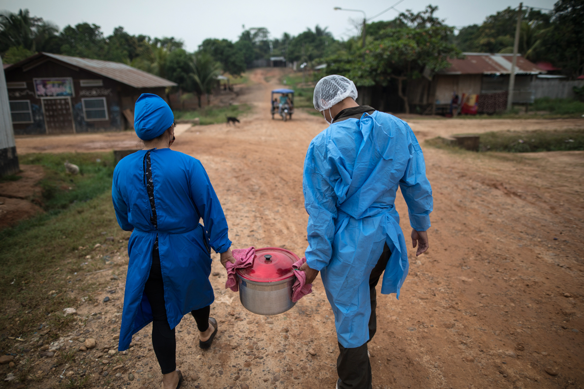 Mery Fasabi, left, and Isai Eliaquin Sanancino, carry a pot of herbs steeped in boiling water to the home of a woman infected with the new coronavirus, in the Shipibo Indigenous community of Pucallpa