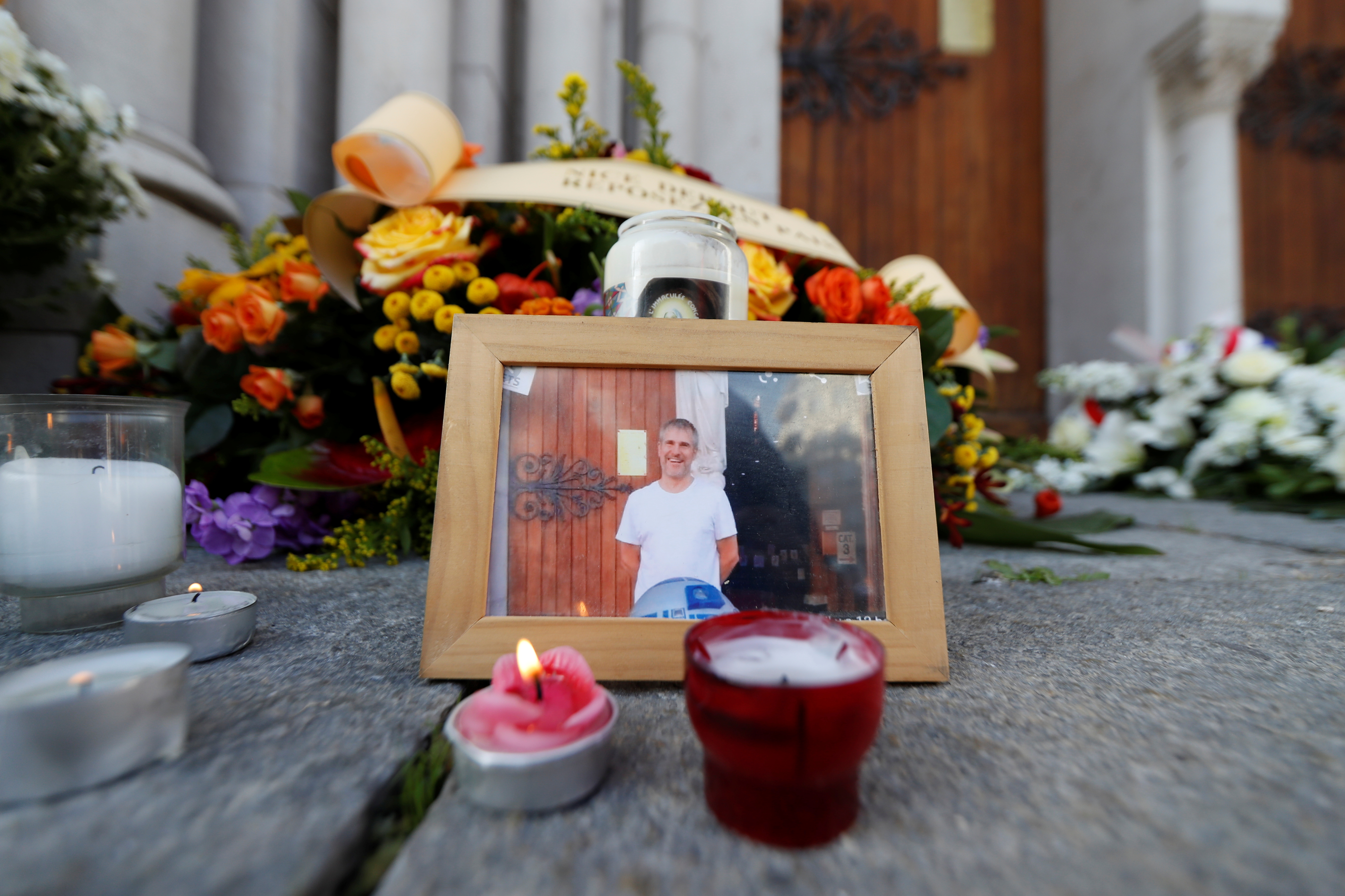 A picture of one of the victims of the knive attack, Vincent Loques, sexton of the Notre Dame church, is seen with candles and flowers outside the church in Nice, France, on October 30, 2020 [Eric Gaillard/Reuters]