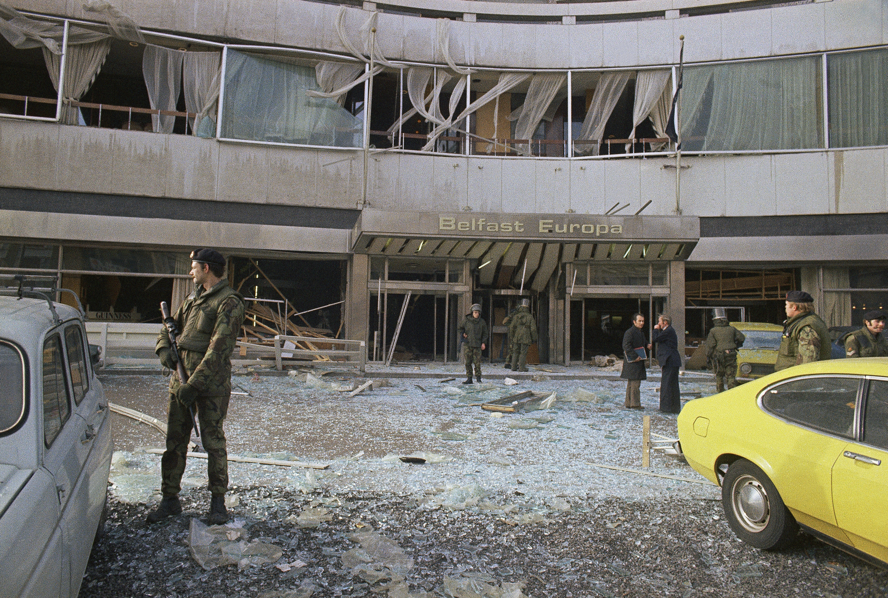 British troops stand guard as bomb experts search through the wreckage after a bomb on the ground floor of the hotel in 1975