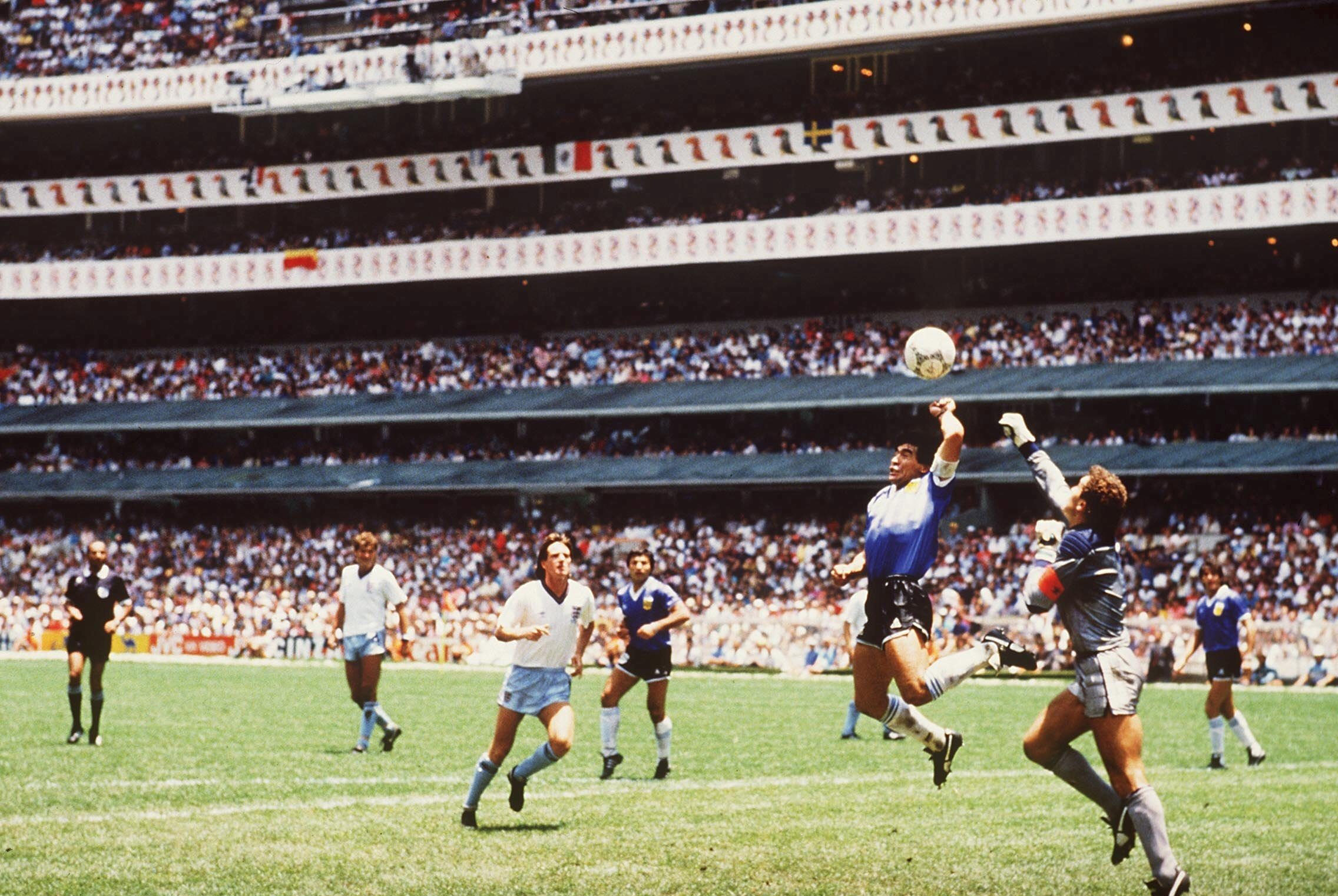 Diego Maradona jumps for the ball with Peter Shilton and handles it