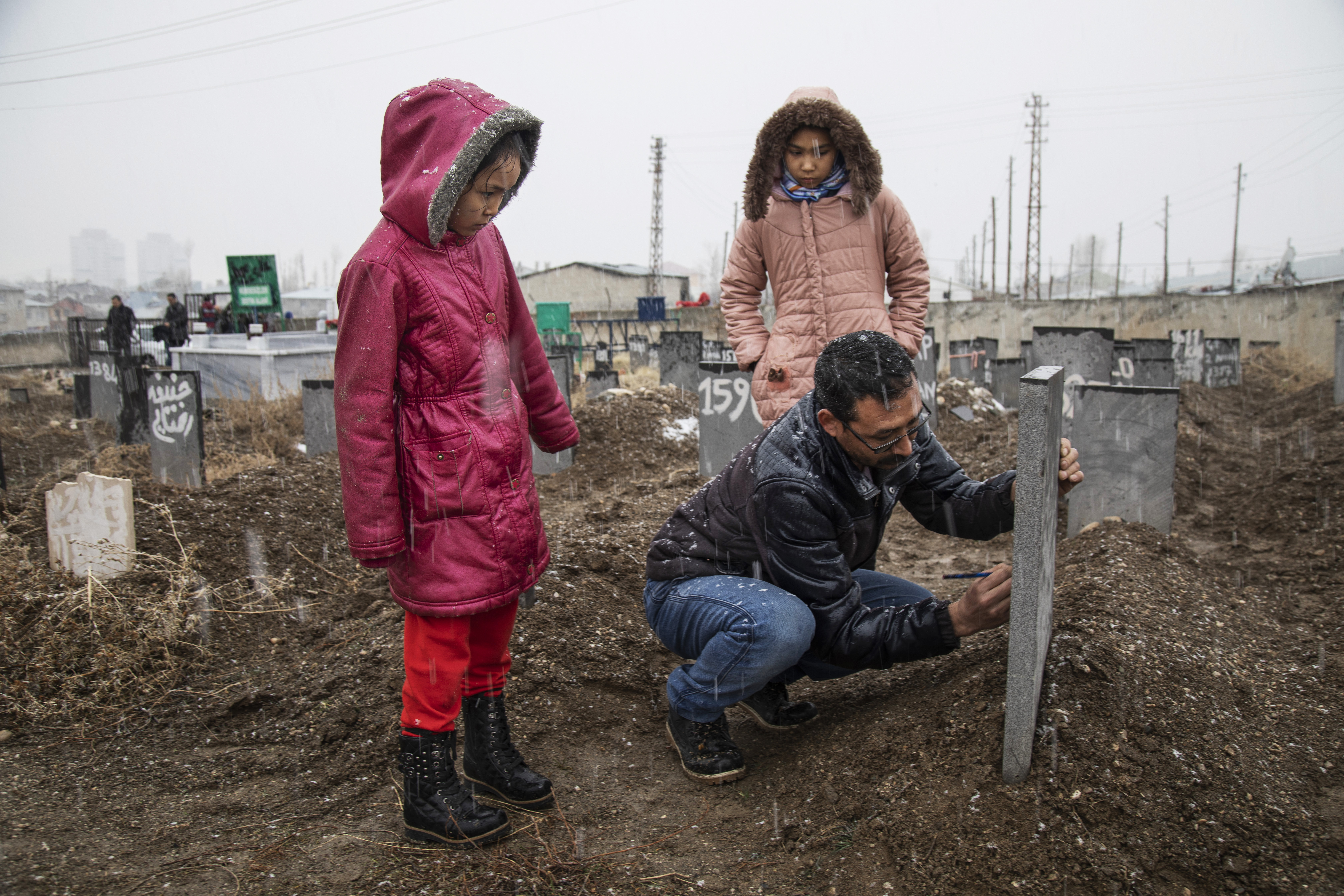 Hamdi Mohseni and his daughters Zeynep and Ferishta visit the grave of Zahra, who died at age four while the family attempted to travel across Turkey towards Europe [Oscar Durand/Al Jazeera]