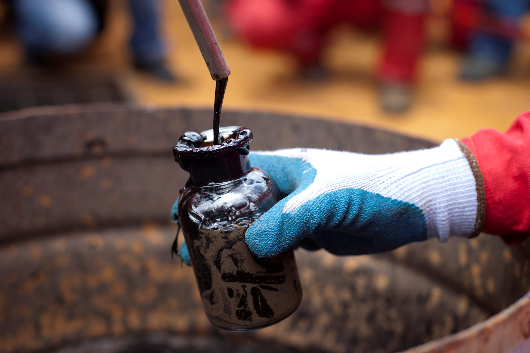 A worker collects a crude oil sample at an oil well.