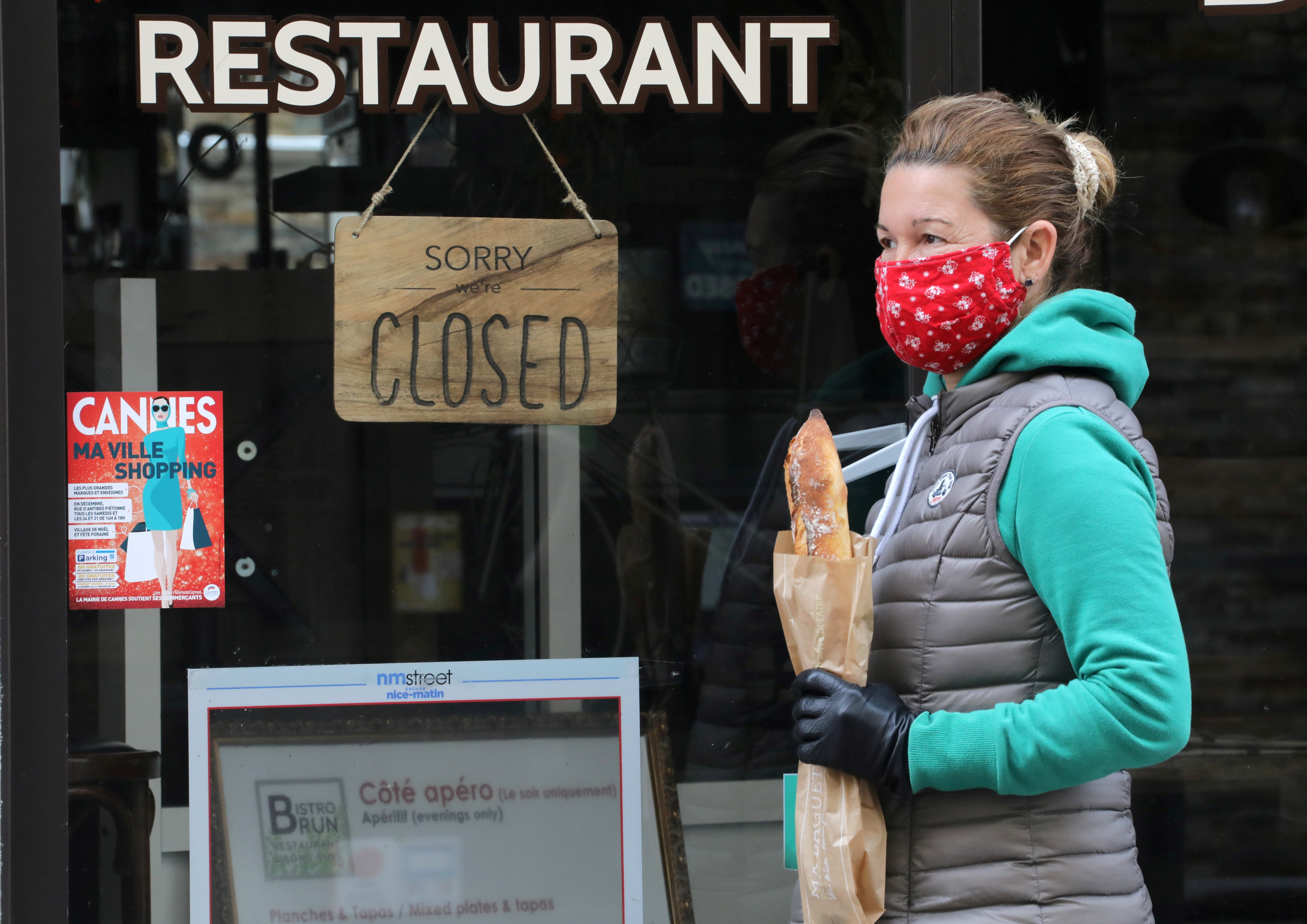 FILE PHOTO: A woman wearing a protective face mask holds a French baguette as she walks past a closed restaurant in Cannes in France, April 16, 2020. REUTERS/Eric Gaillard/File Photo