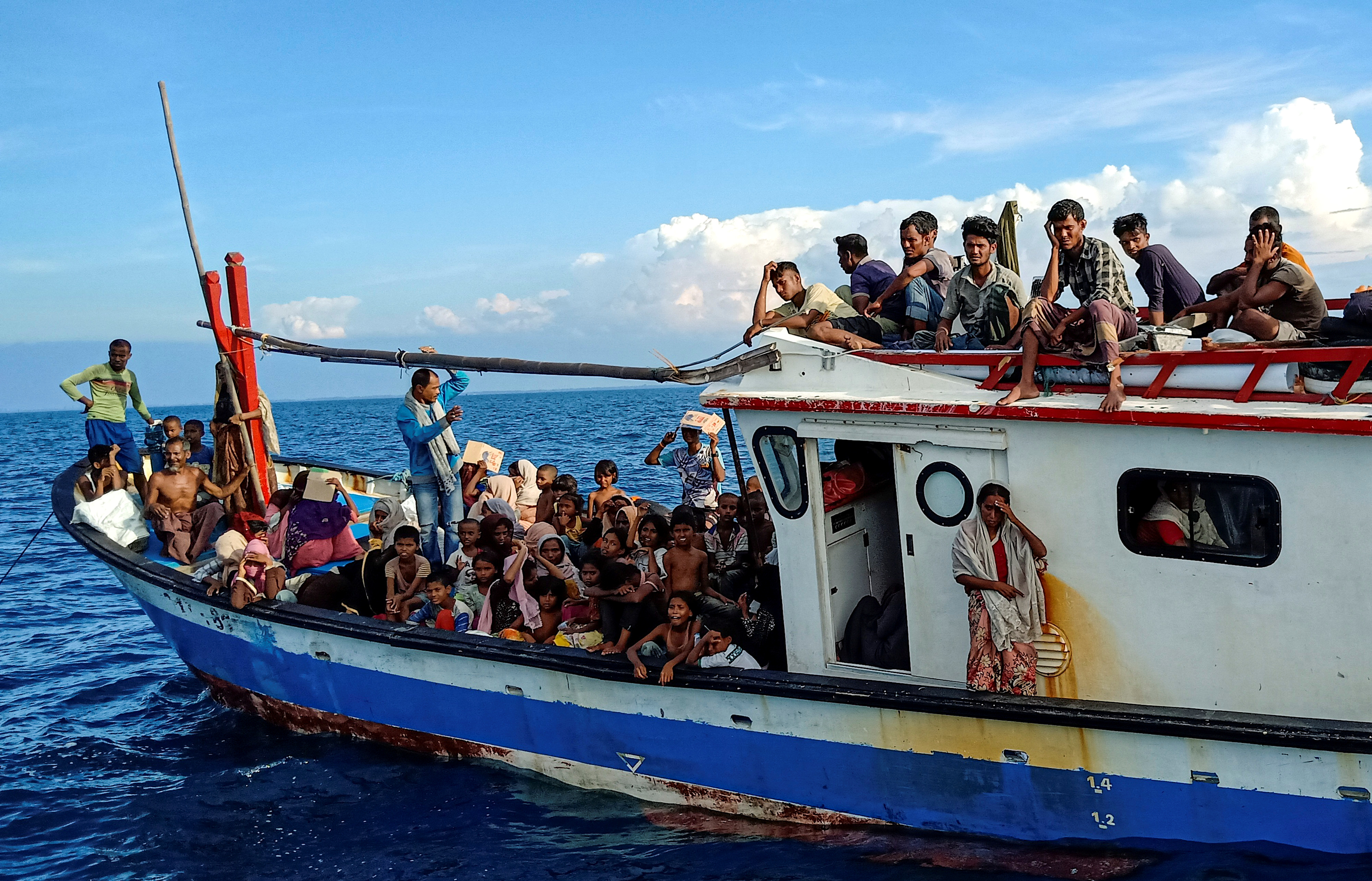 Rohingya refugees packed onto the deck of a wood fishing boat. Some are sitting on top of the wheelhouse.