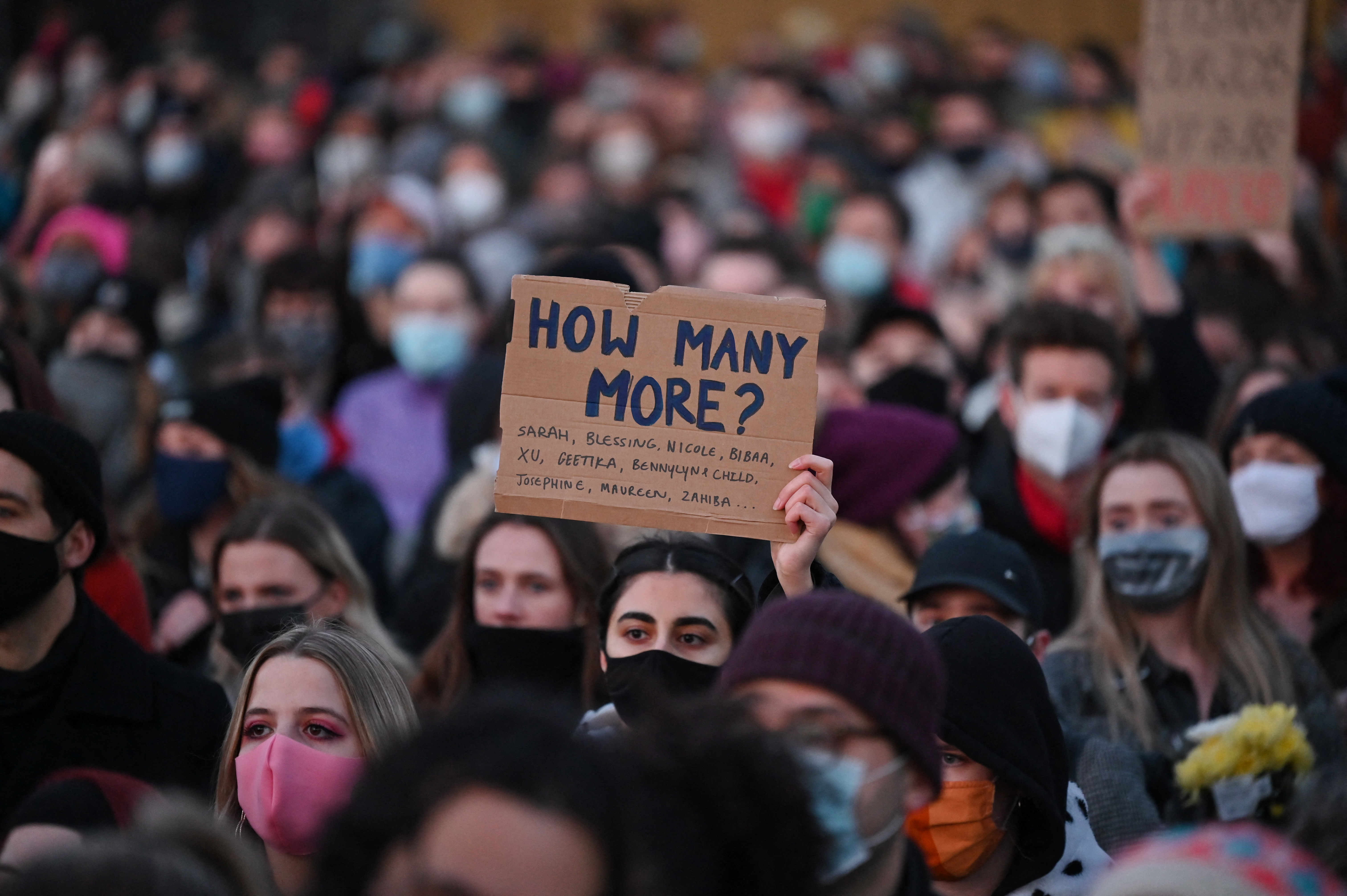 Well-wishers, one with a placard that reads 'How many more', gather at the band-stand where a planned vigil in honour of alleged murder victim Sarah Everard which was officially cancelled due to COVID-19 restrictions, was to place on Clapham Common, south London, March 13, 2021 [Justin Tallis/AFP]