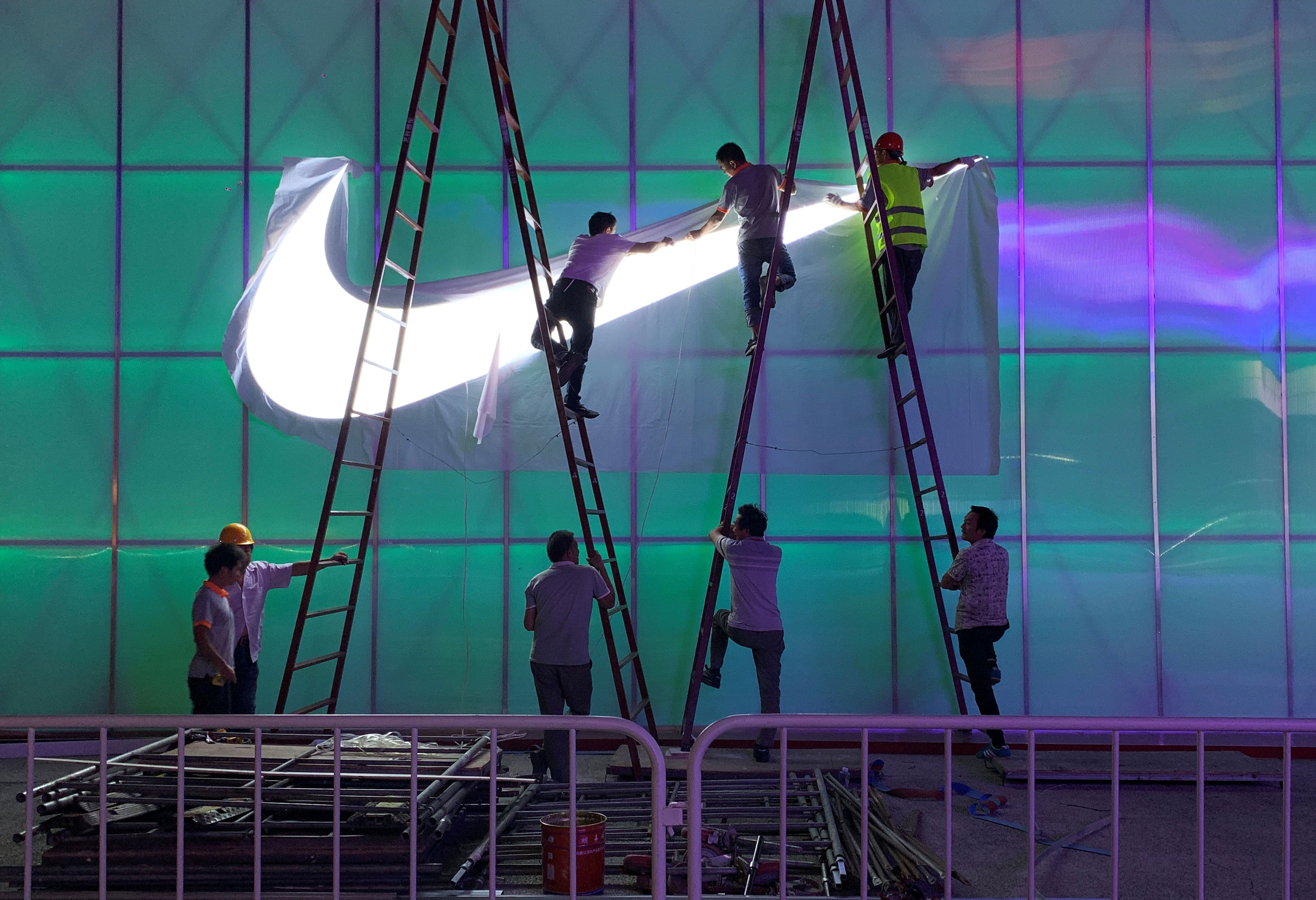 Workers install a Nike logo lamp outside the Wukesong Arena in Beijing, China [File: Tingshu Wang/Reuters]