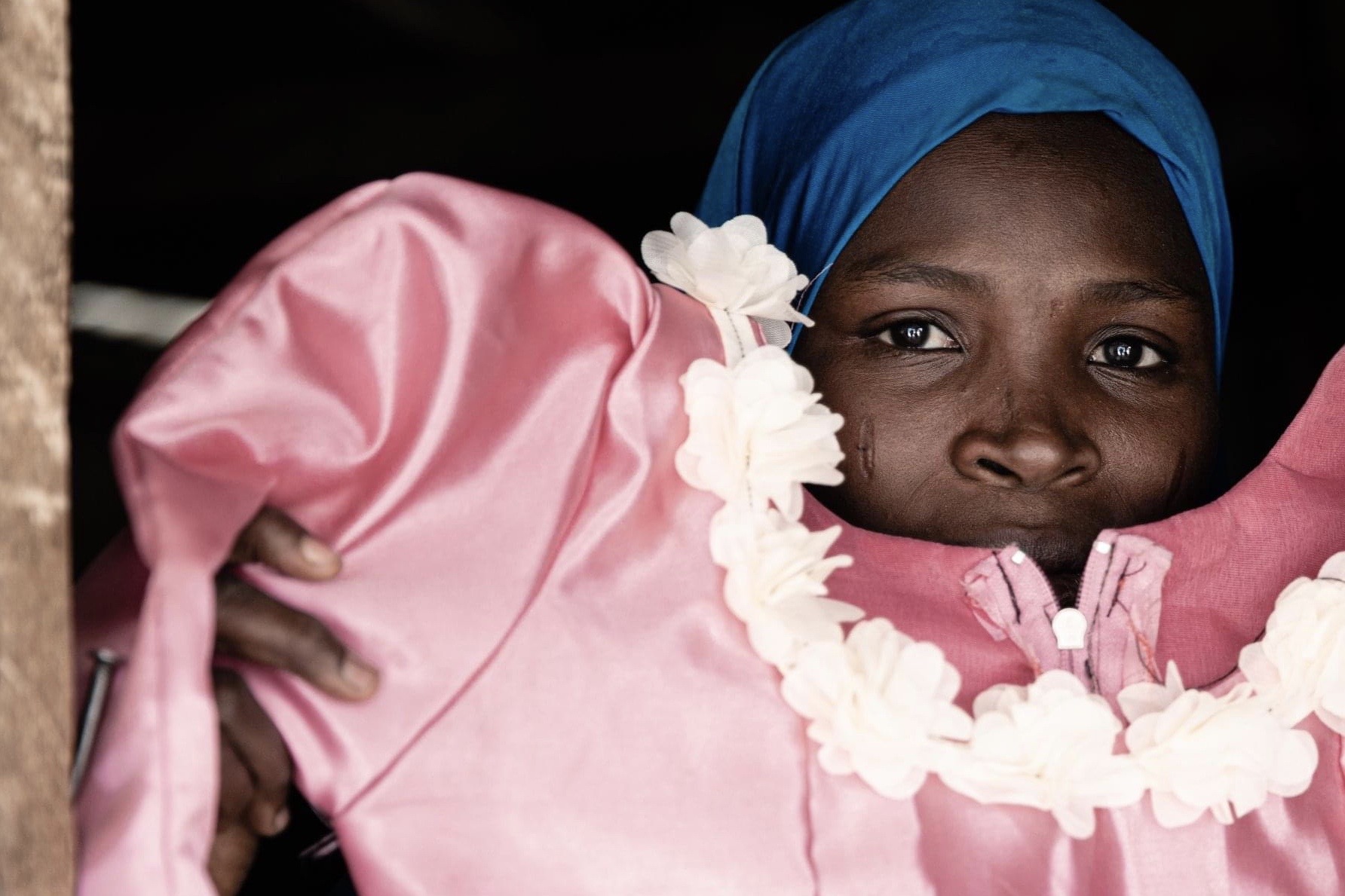 Aisha, a dressmaker in Dalori displacement camp, shows off the pink dress with white flowers she made. [Alyona Synenko/ICRC]