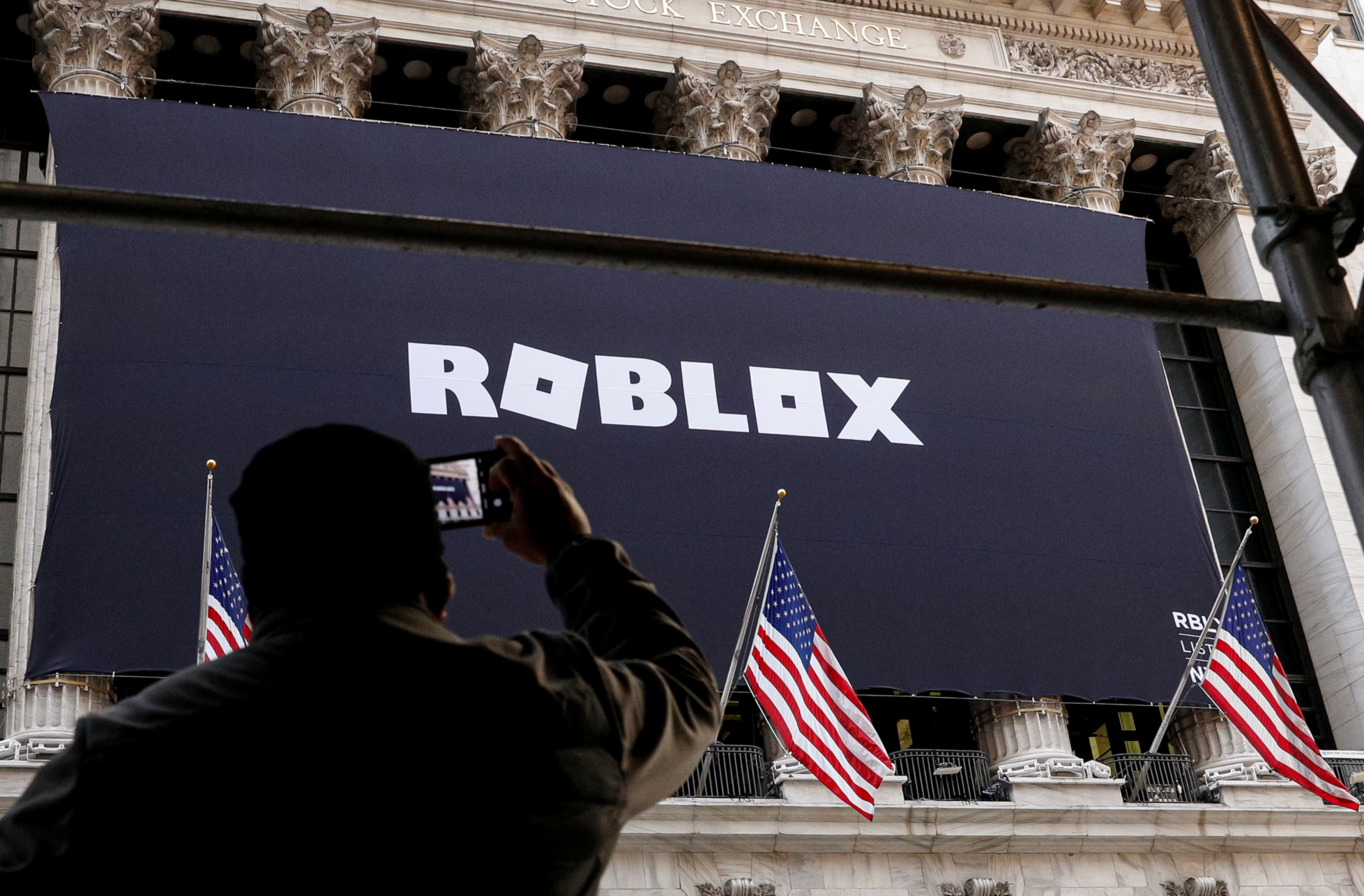 A man photographs a Roblox banner hanging on a building.
