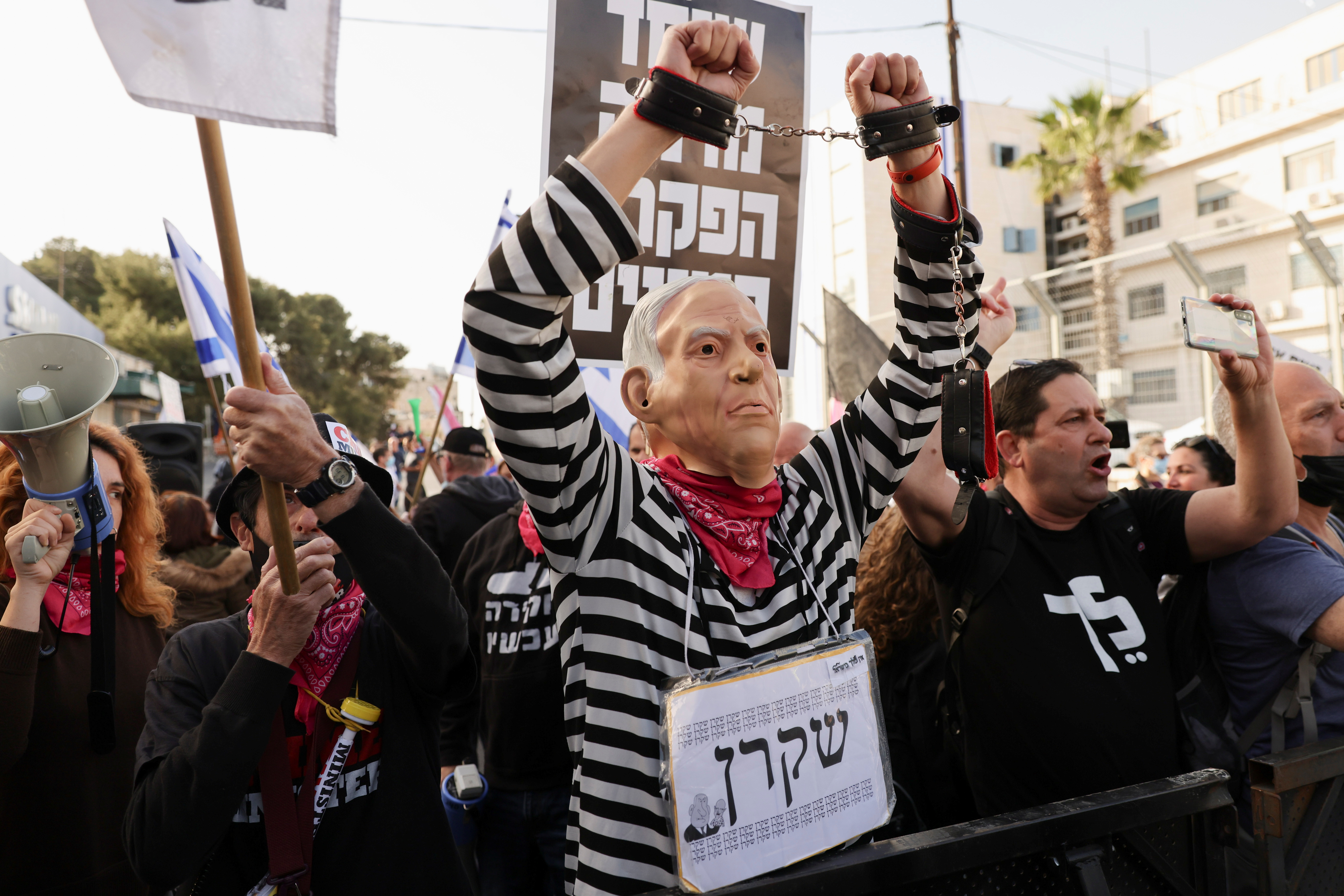 A protester wearing a mask depicting Israeli Prime Minister Benjamin Netanyahu and a sign with the word "Liar" in Hebrew, gestures during a demonstration against Netanyahu before his corruption trial resumes, near Jerusalem's District Court April 5, 2021. REUTERS/Ronen Zvulun