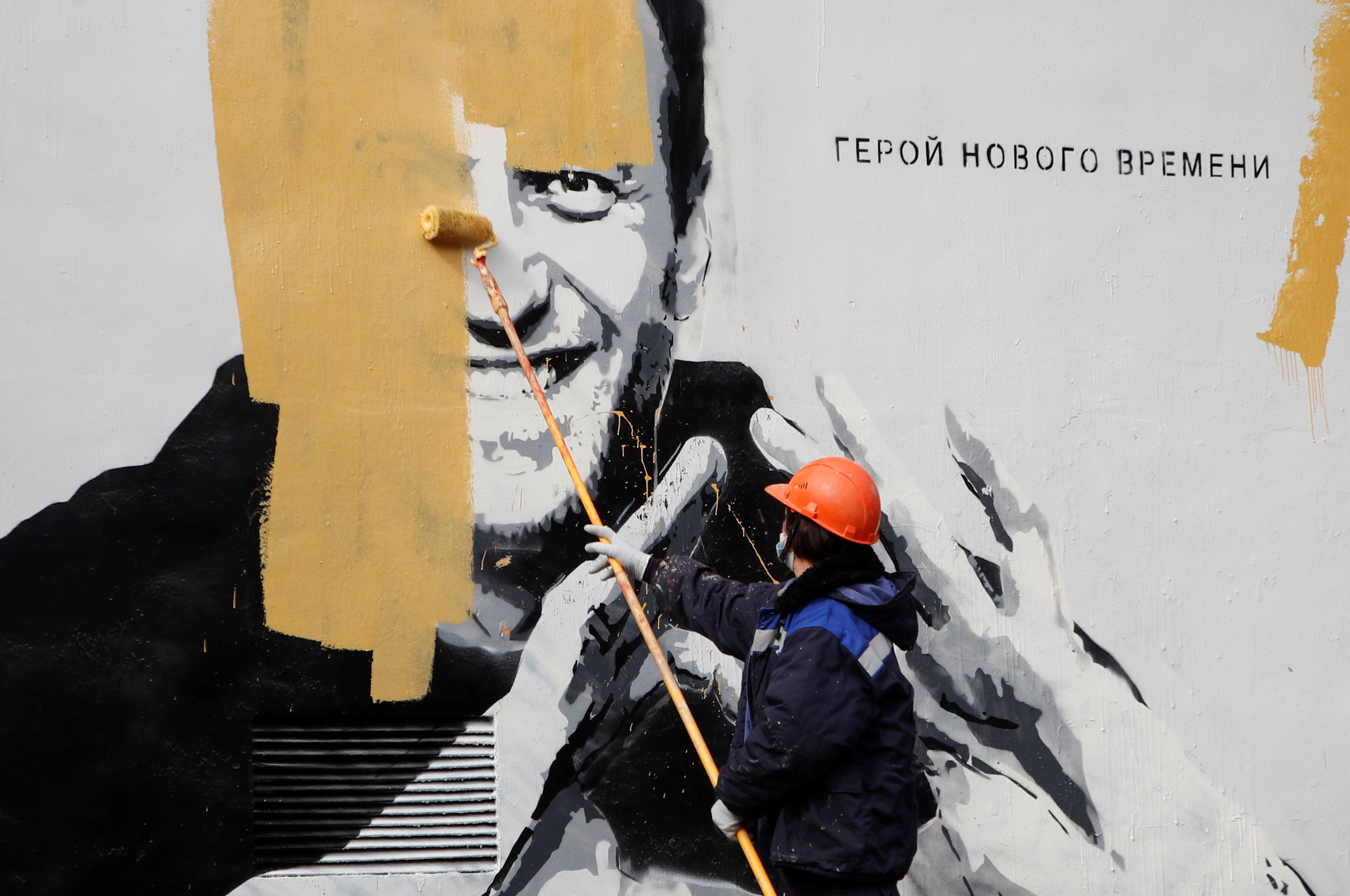 A worker paints over a graffiti depicting jailed Russian opposition politician Alexei Navalny in Saint Petersburg