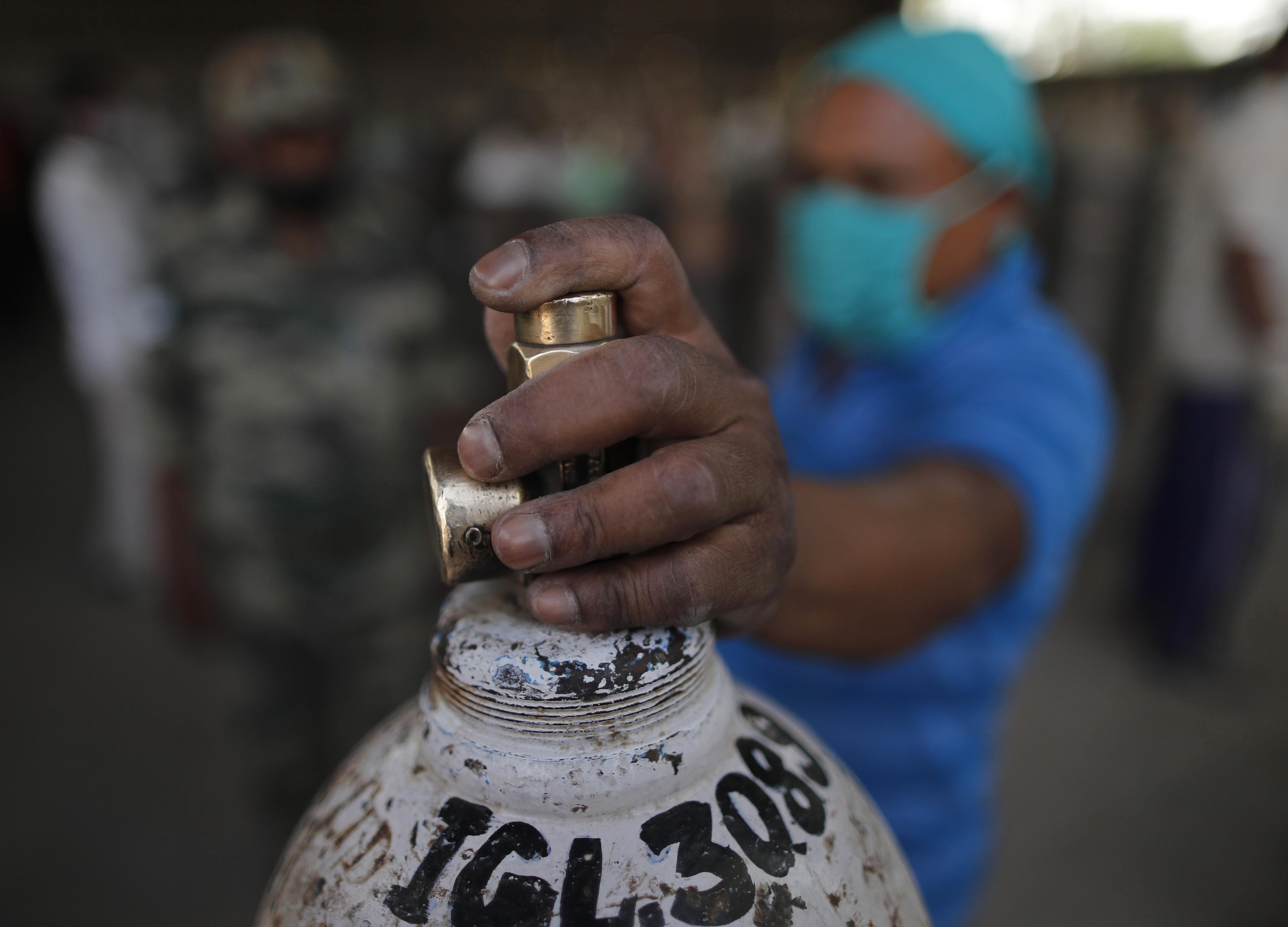 A man waits to refill a medical oxygen cylinder at a charging station on the outskirts of Prayagraj, India, on April 23, 2021 [Rajesh Kumar Singh/AP Photo]