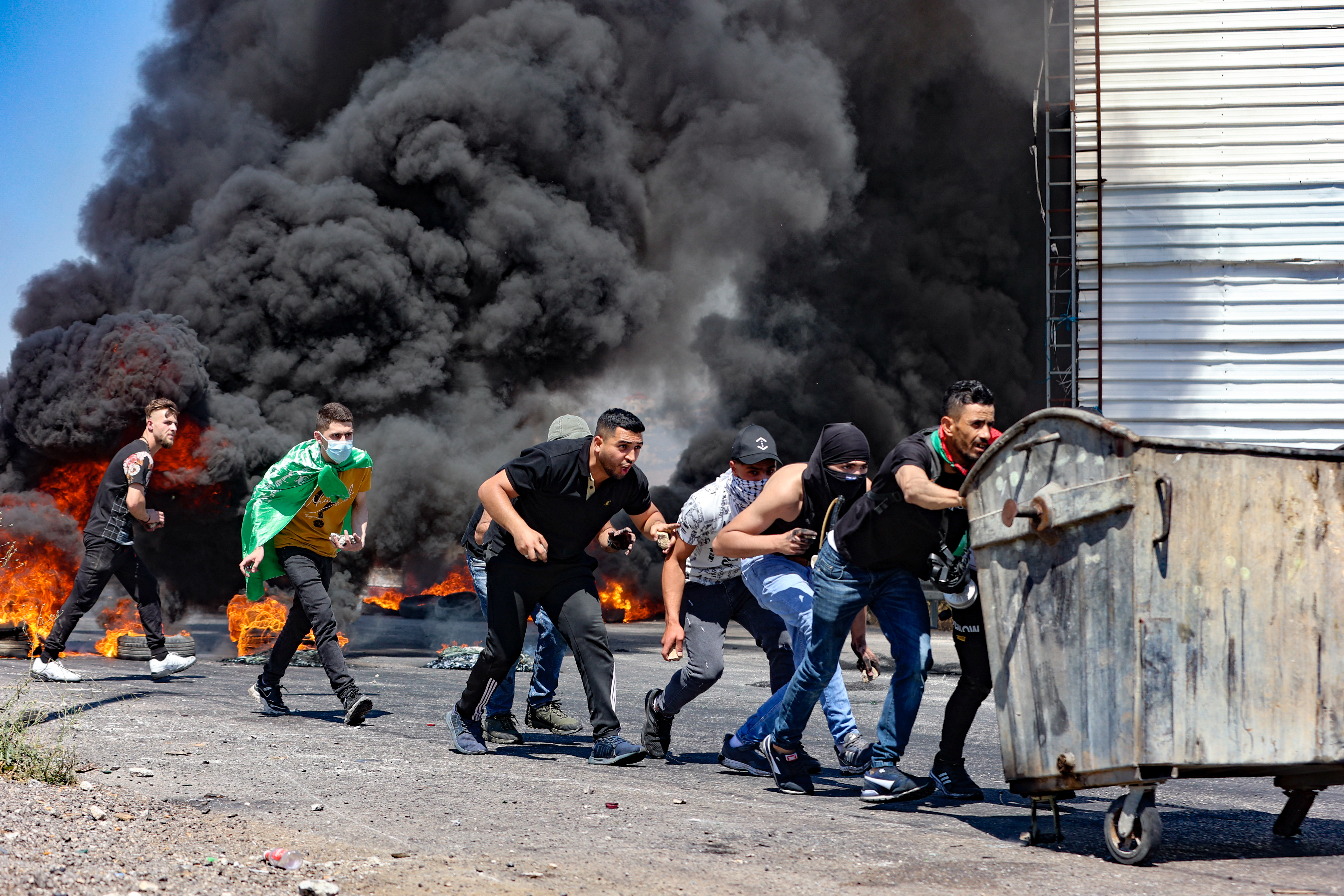 Palestinian youths use a rubbish bin as a barricade, during confrontations with Israeli security forces near the Hawara checkpoint south of the occupied West Bank city of Nablus [Jaafar Ashtiyeh/AFP]