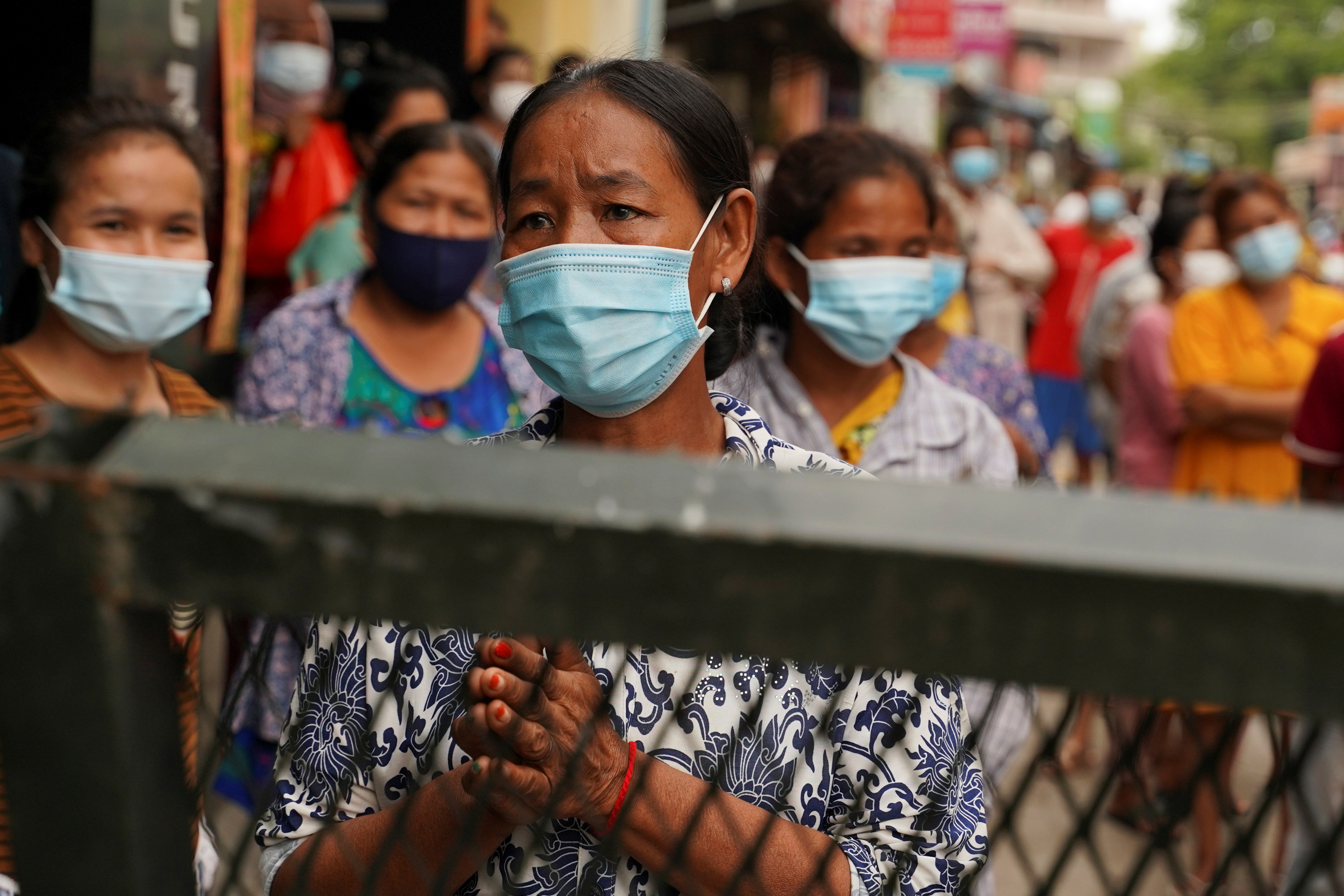 Villagers stand behind a lockdown barrier to ask for food donations after their village has been closed for more than two weeks inside a red zone with strict lockdown measures during the latest outbreak of COVID-19 in Phnom Penh, Cambodia, April 30, 2021 [Cindy Liu/Reuters]