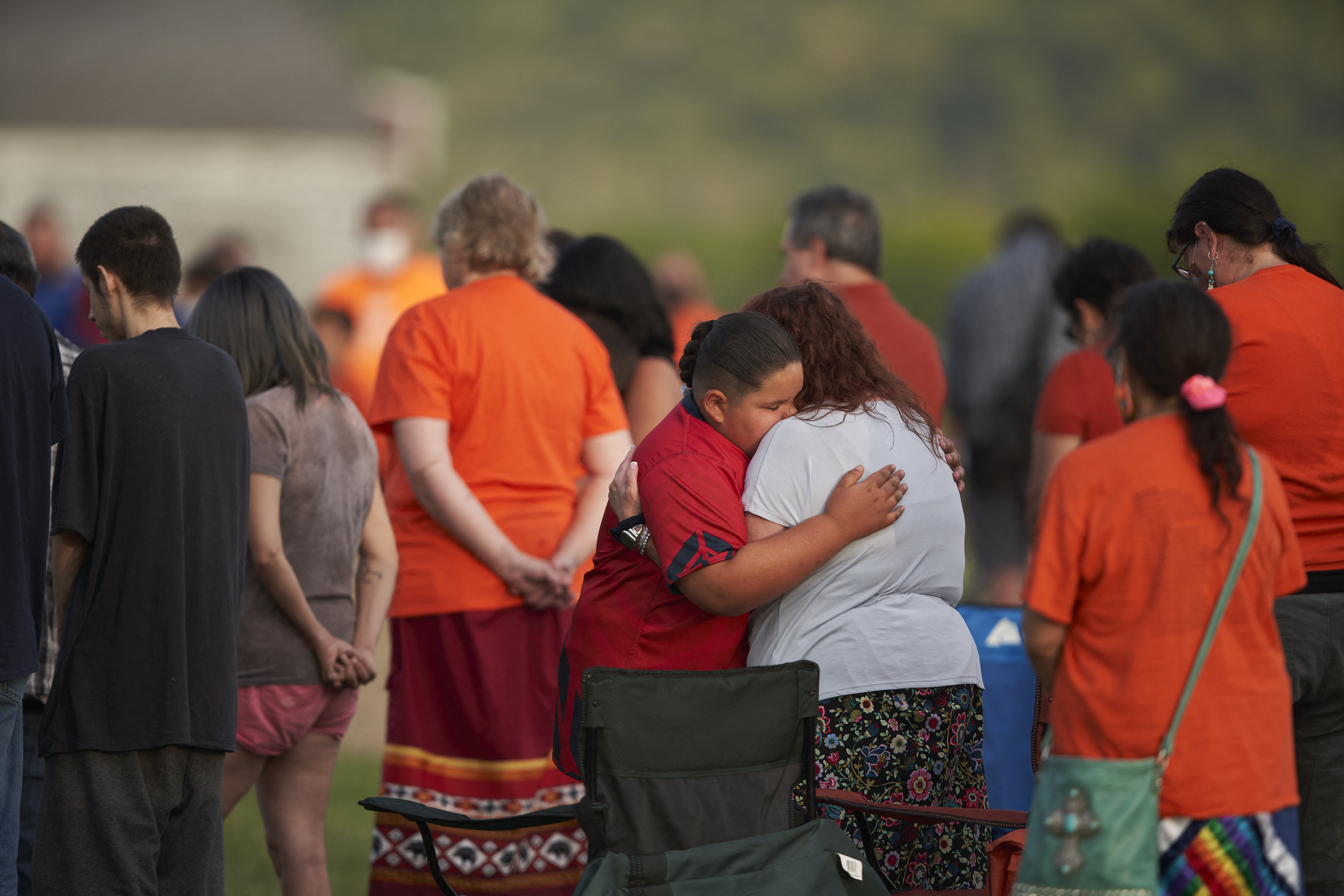 people hug in a field where unmarked graves were discovered