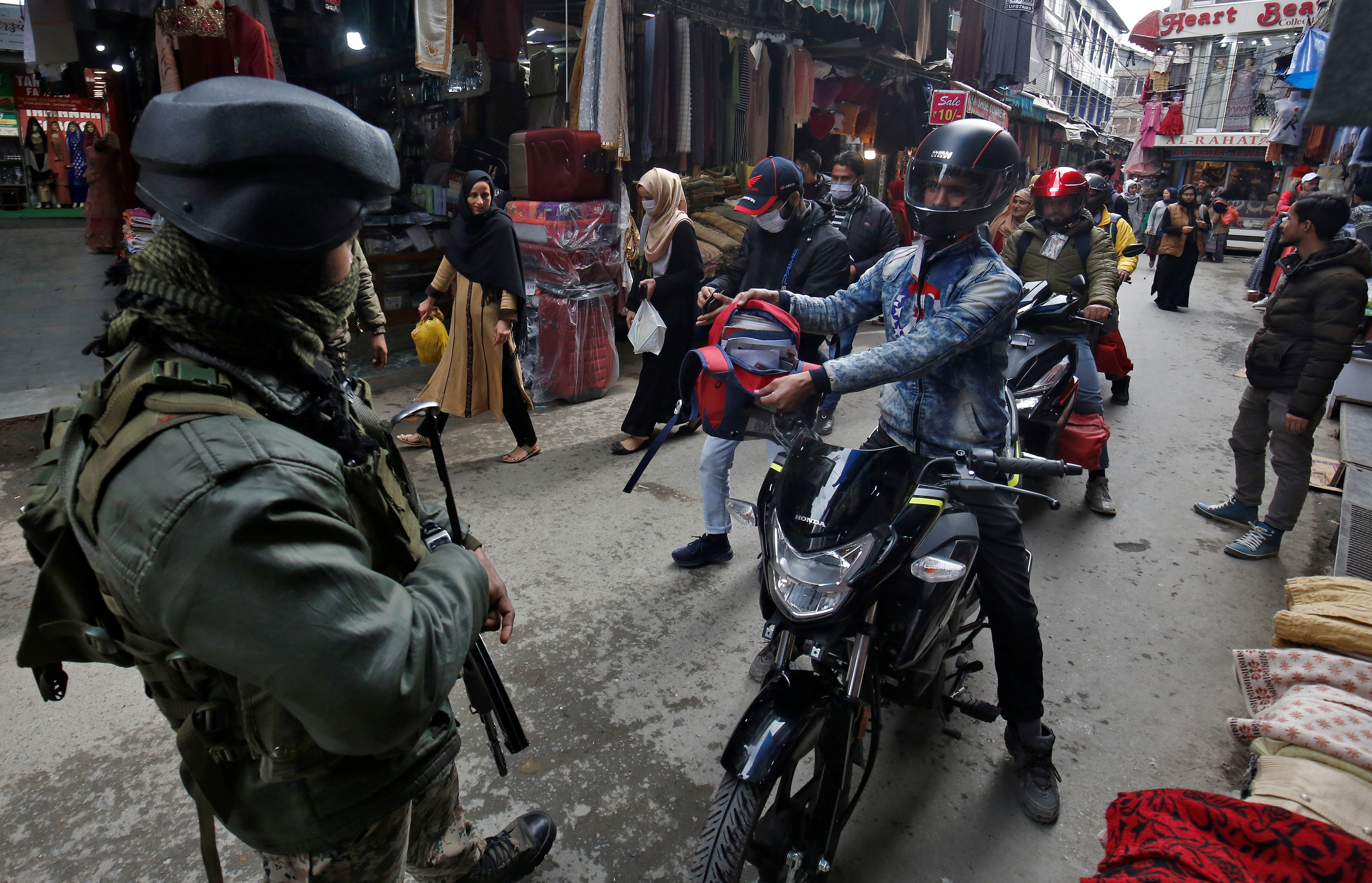 A man on a motorbike shows the contents of his bad to an Indian security force personnel at a marketplace during a cordon and search operation, in Srinagar on February 26, 2021 [Reuters/Danish Ismail]