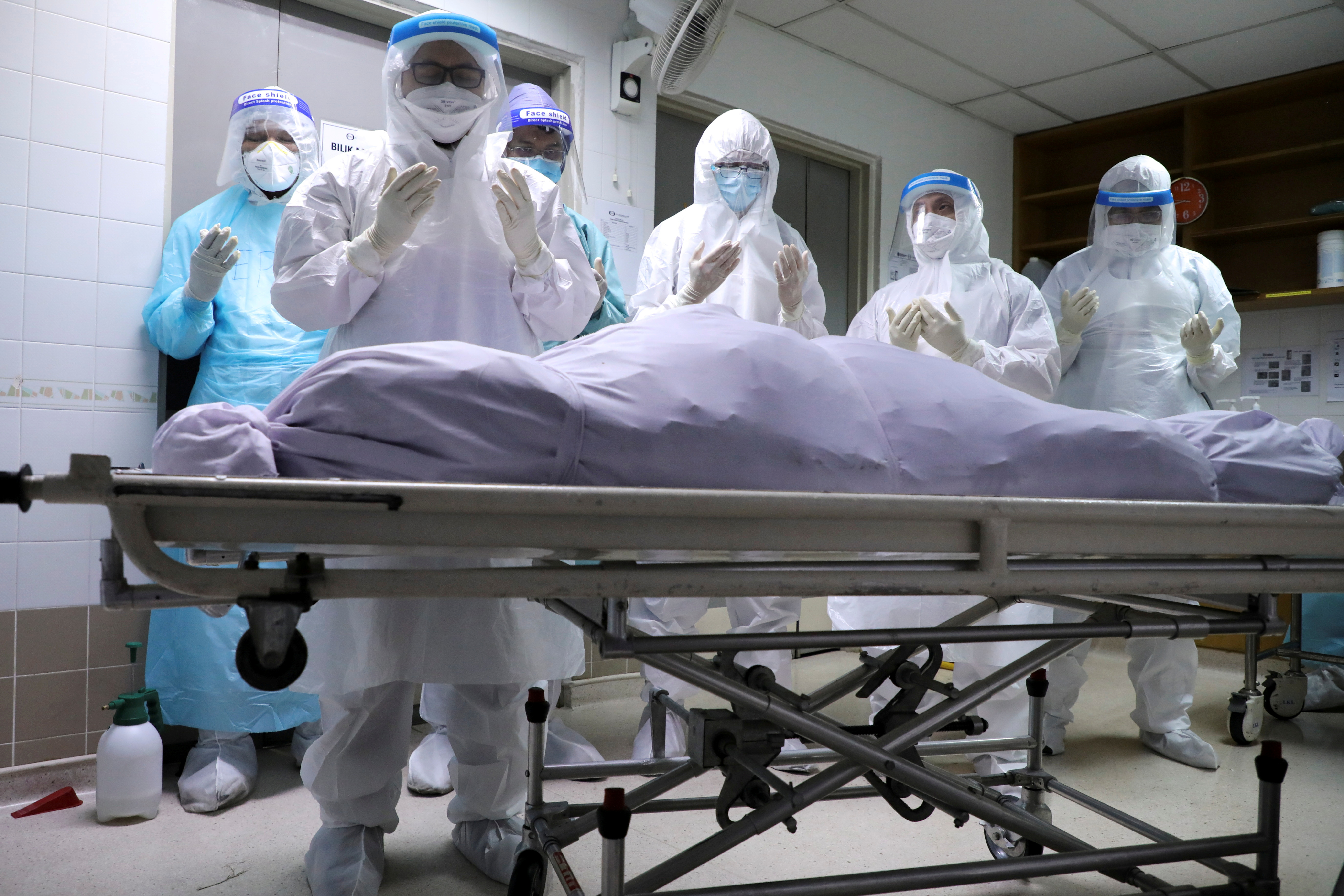 Family members of a victim of COVID-19 pray at a hospital mortuary before burial, in Kuala Lumpur, Malaysia on May 23, 2021 [Reuters/Lim Huey Teng]
