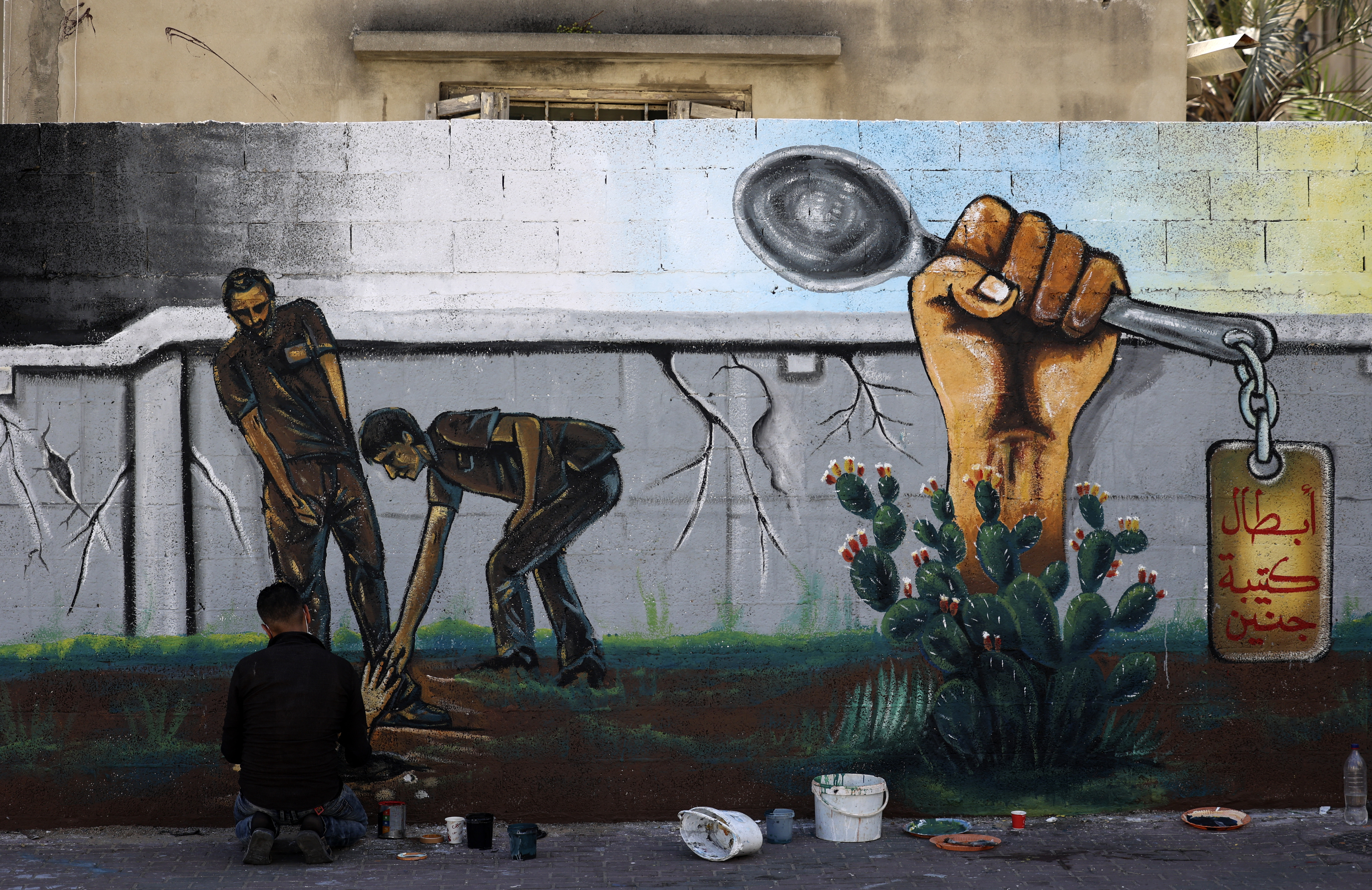 An artist works on a mural painting glorifying six Palestinian prisoners who escaped from Israel's Gilboa prison in September 2021 with the help of the humble spoon [Mahmud Hams/AFP]