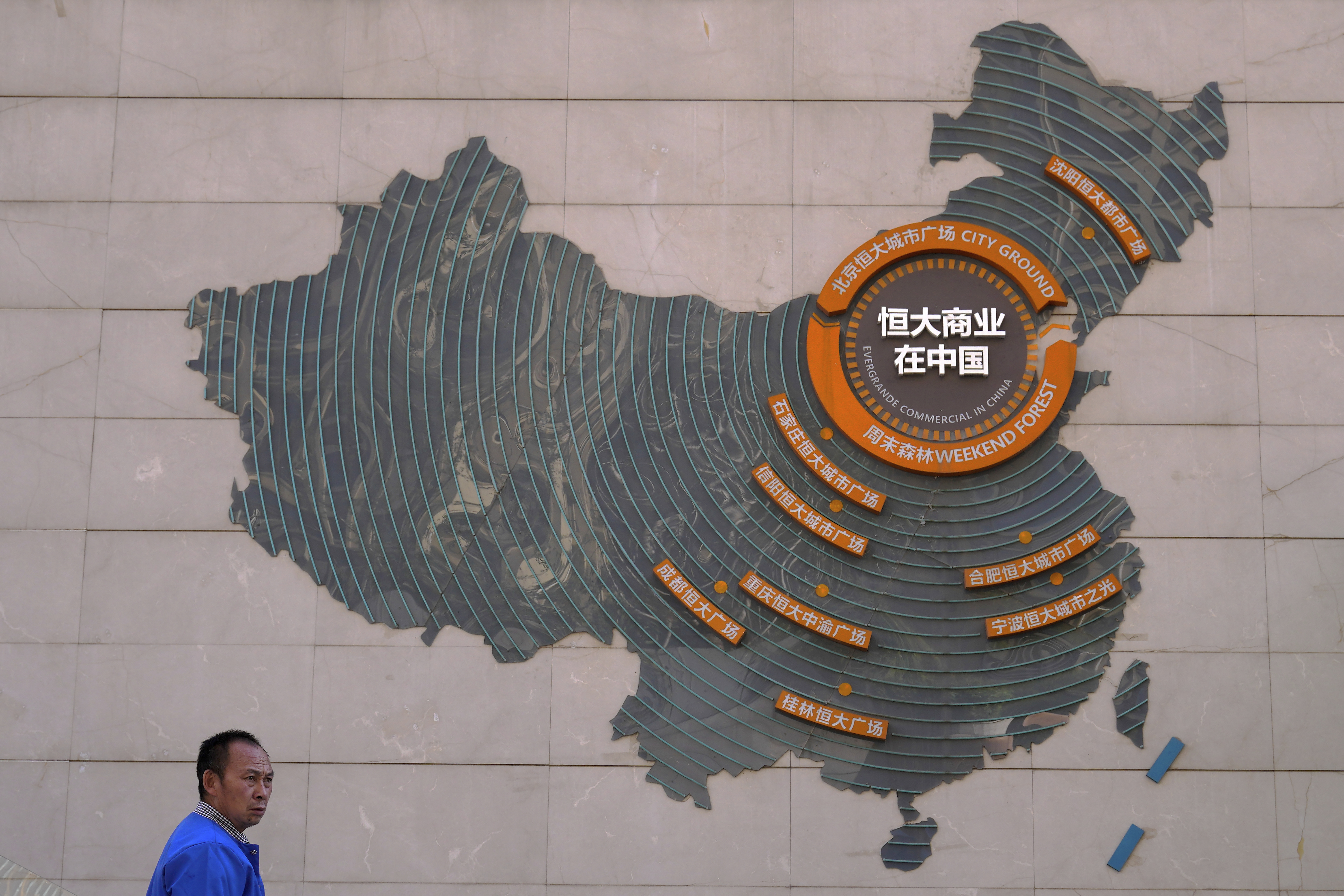A custodian stands near a map of Evergrande's China development projects, in Beijing. Global investors are watching nervously as Evergrande struggles to avoid defaulting on tens of billions of dollars of debt, fuelling fears of possible wider shock waves for the Chinese financial system [Andy Wong/AP Photo]