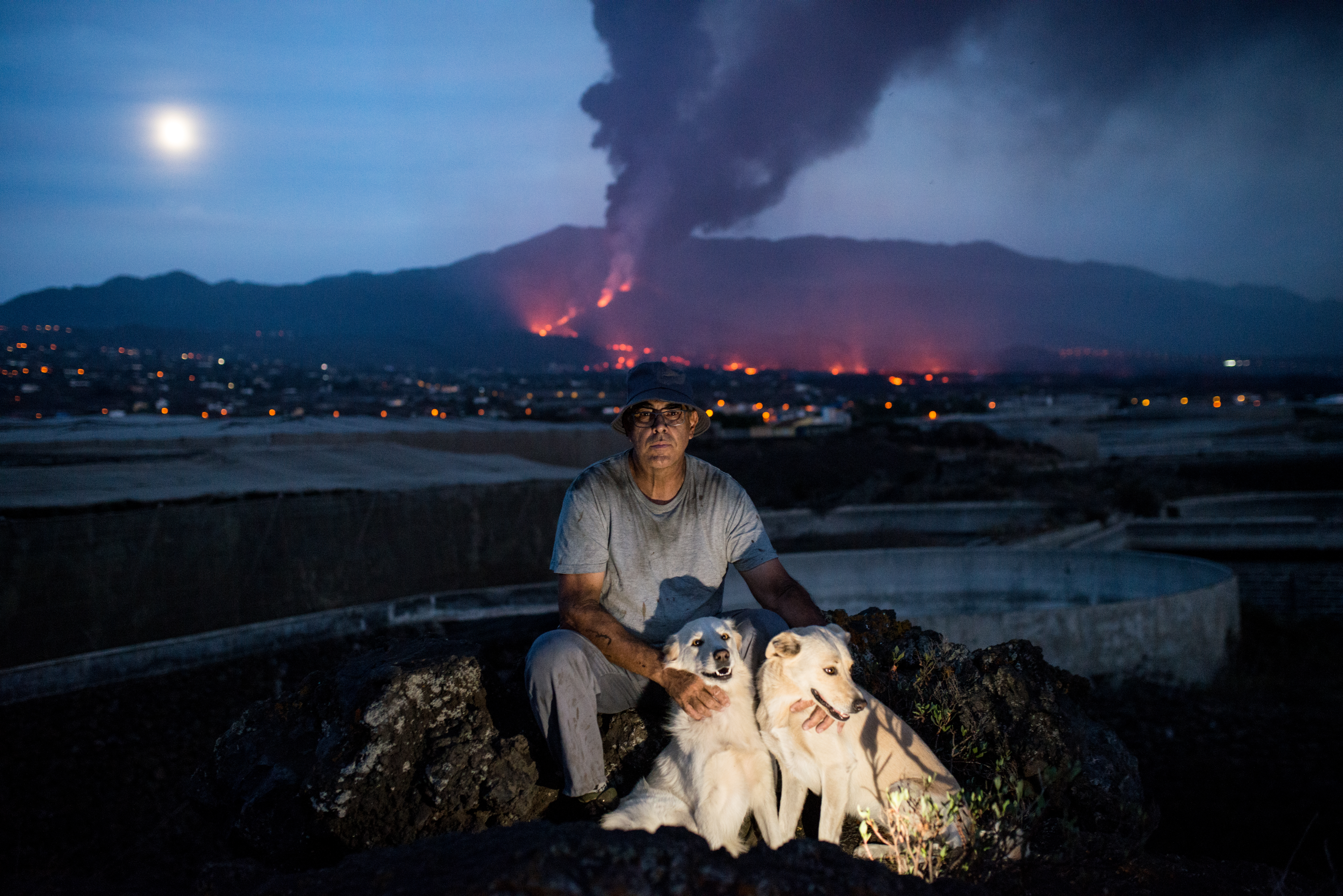 Banana farmer Jose Alvaro Leon Diaz rests with his dogs at the end of a day spent trying to salvage his crop from the ashfall. 'When we try to sell them it looks like the bananas have been sanded down. Inside it’s the same, it’s tasty. But on the outside, to the eye, it doesn't sell.' [Alexander Lerche/Al Jazeera]