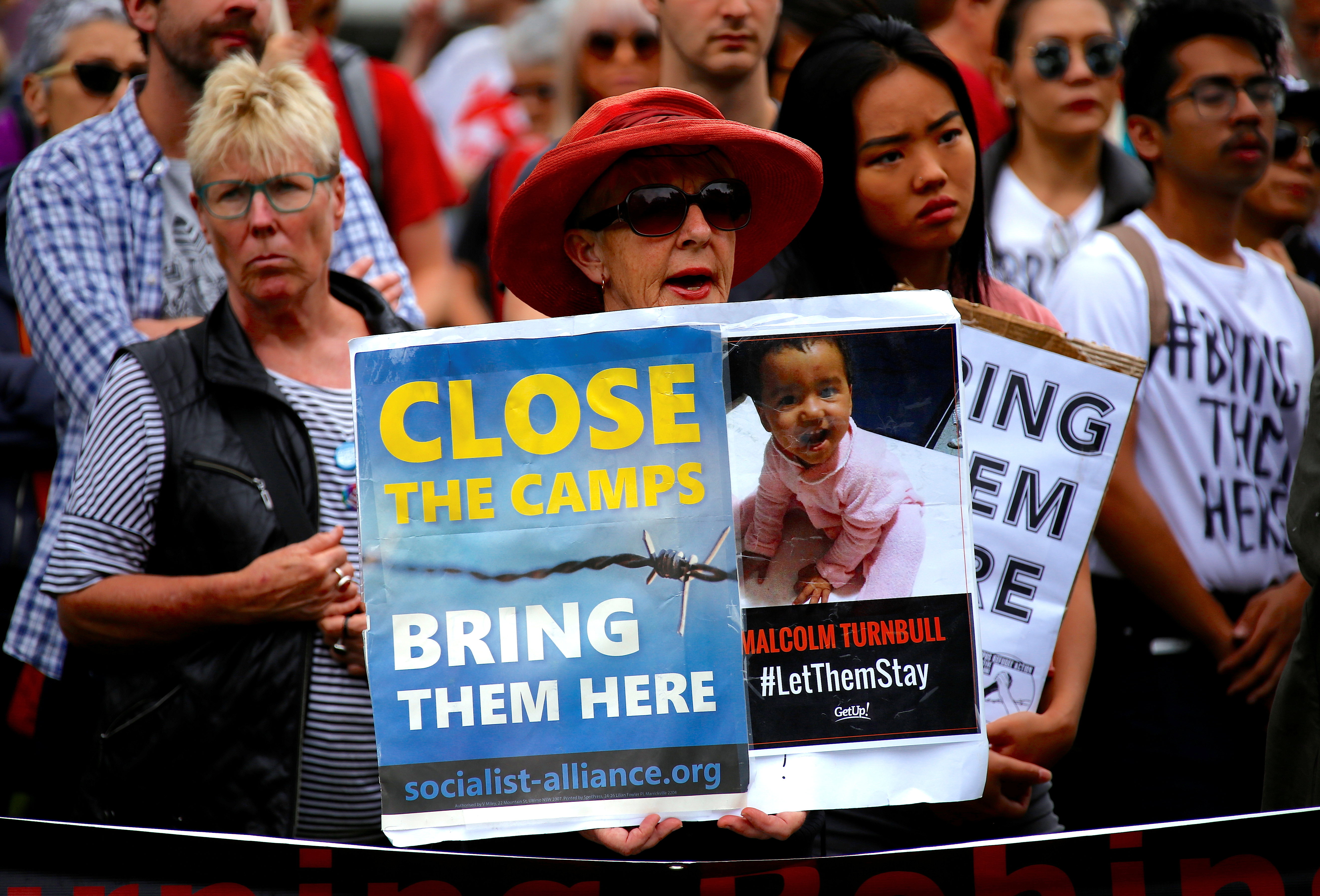 Protesters holding a rally calling for the closure of Manus and Naurou. The placards say 'close the camps, bring them here'. One shows a picture of a small child.